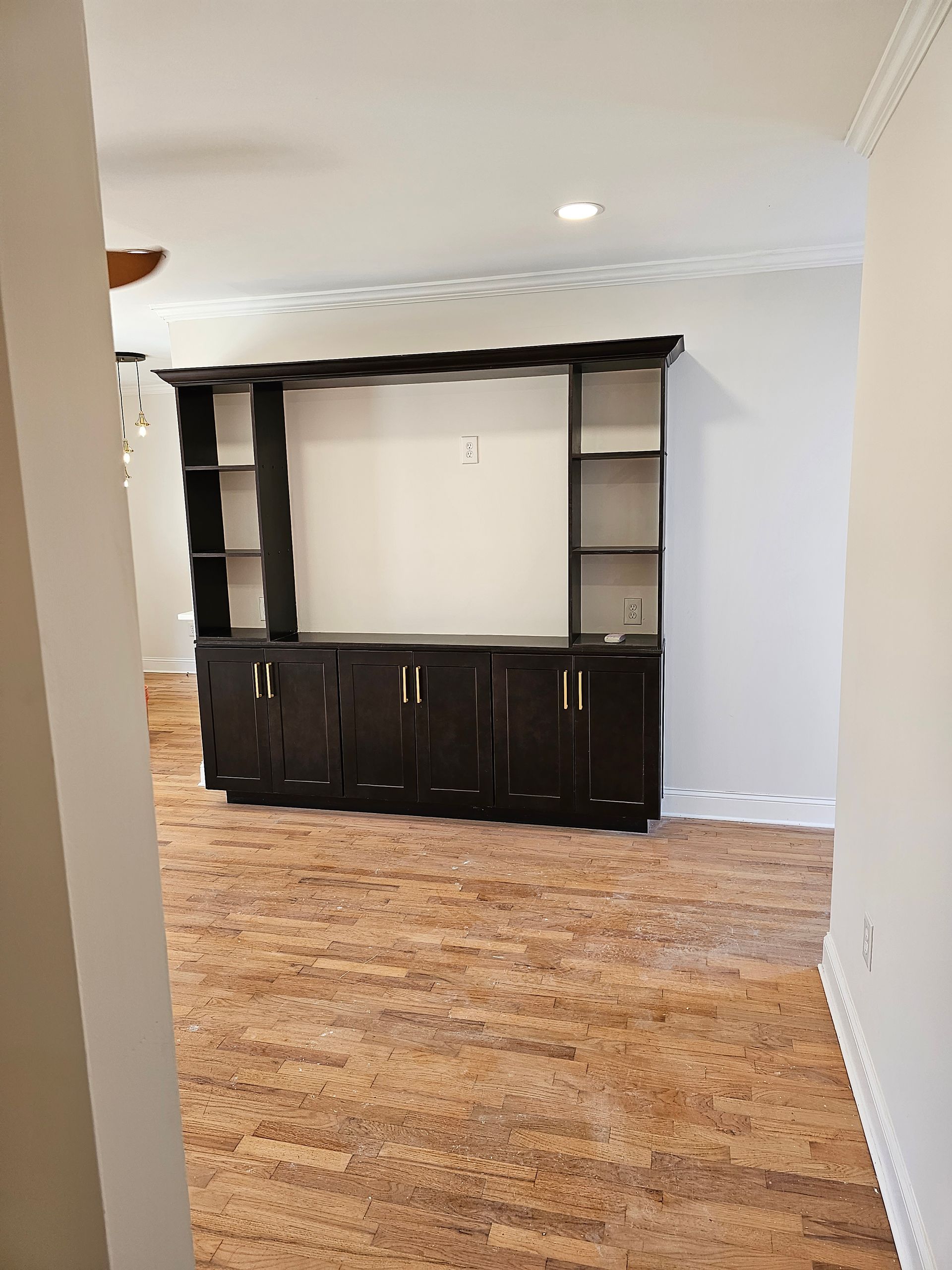 Dark brown entertainment center with open shelves and cabinets, against a white wall and tan patterned flooring.