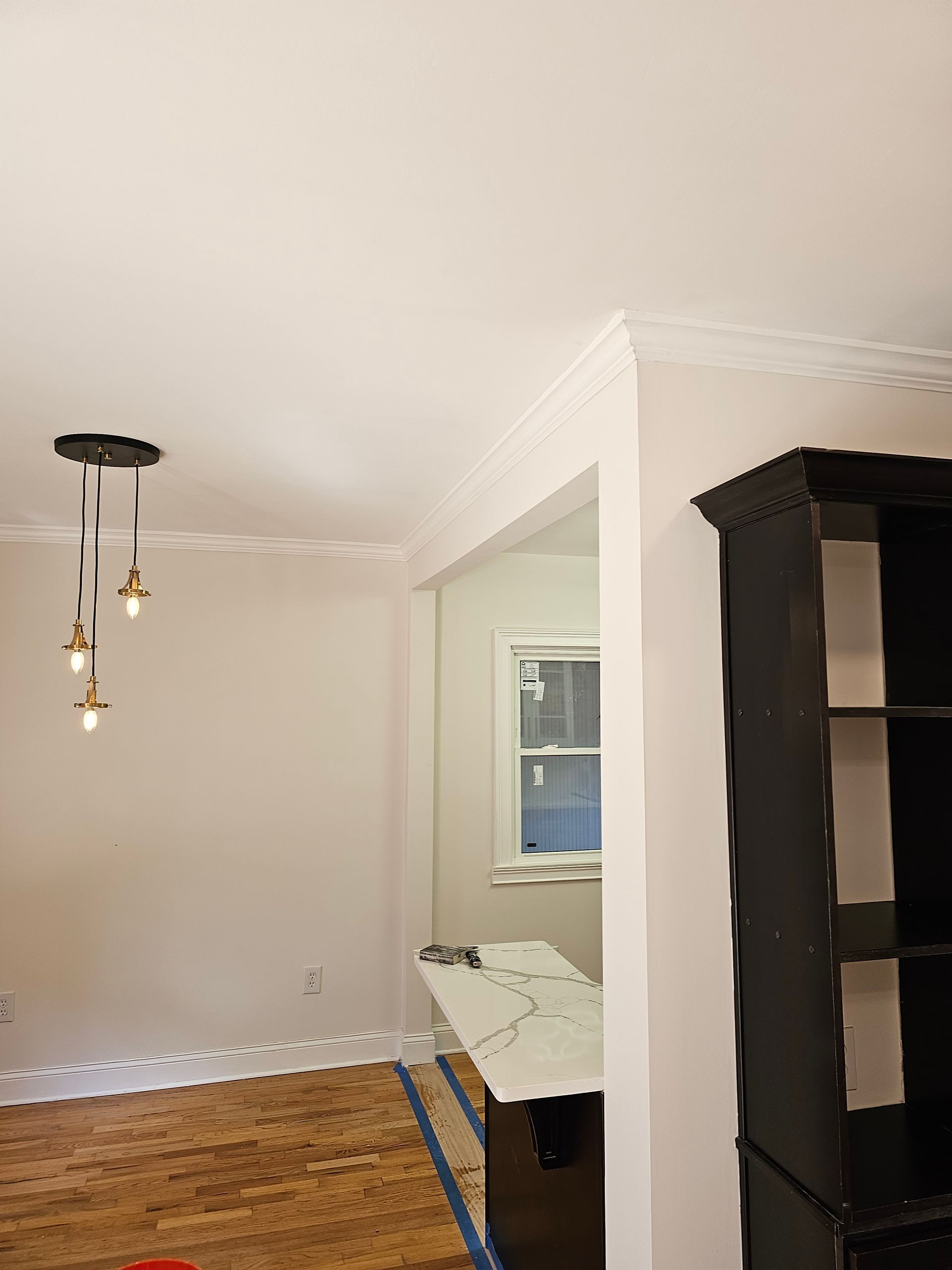 Dining room interior with crown molding, pendant lights, wooden floor, and a black storage unit.
