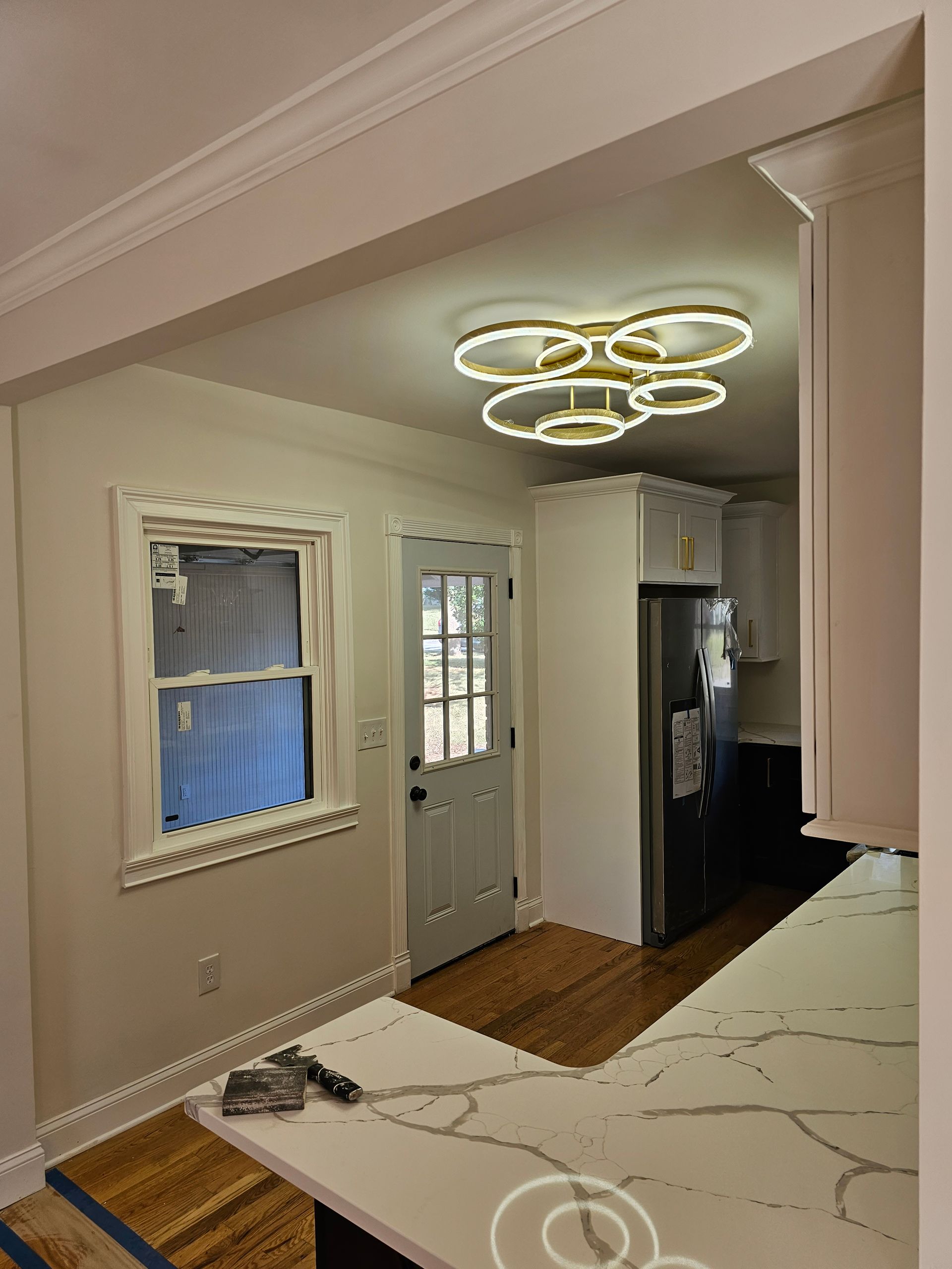 Kitchen with white cabinets, quartz countertop, and a decorative ceiling light. Door and window visible.