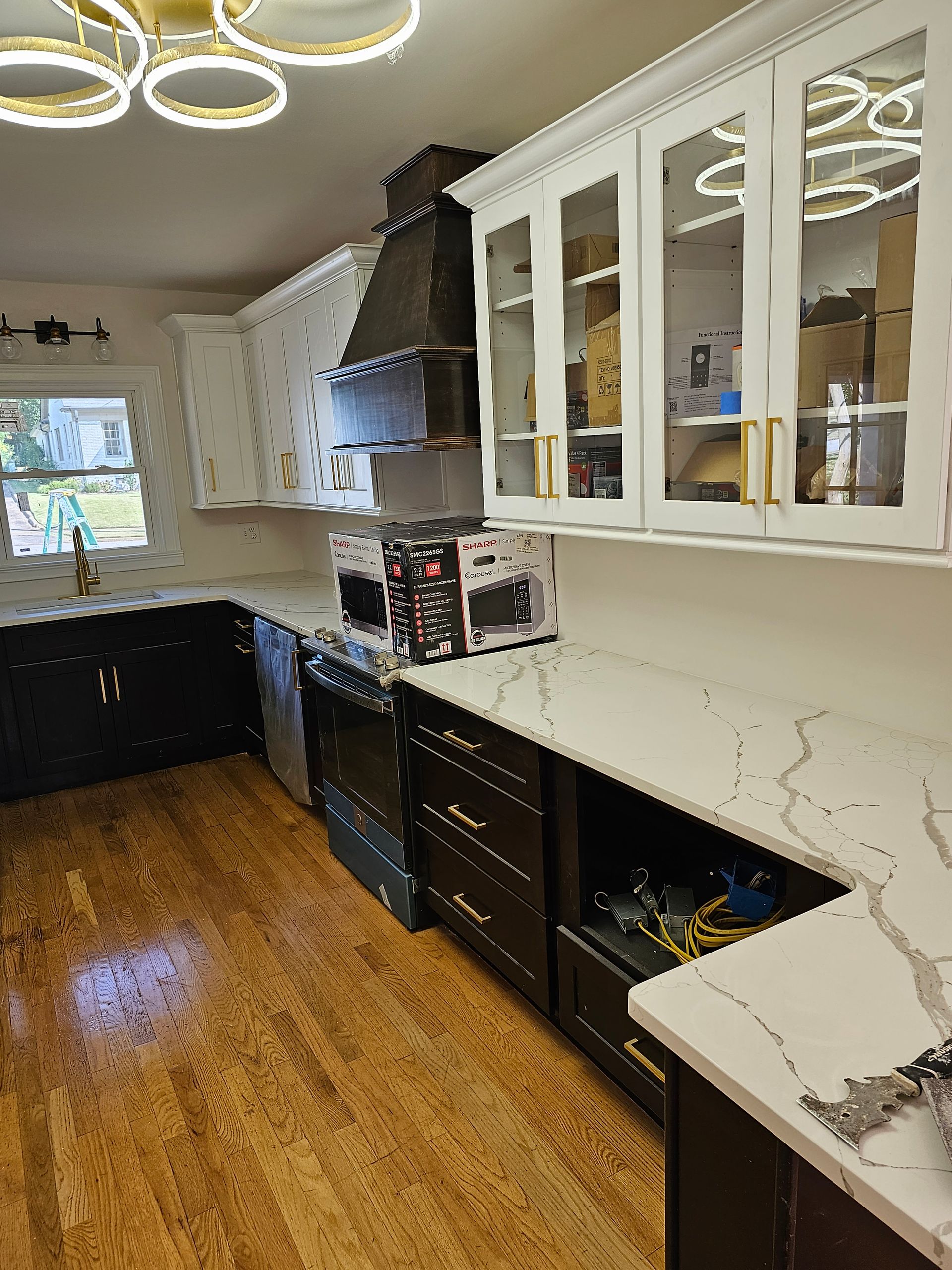 Kitchen with white and dark cabinets, quartz countertops, stainless steel hood, and gold hardware.