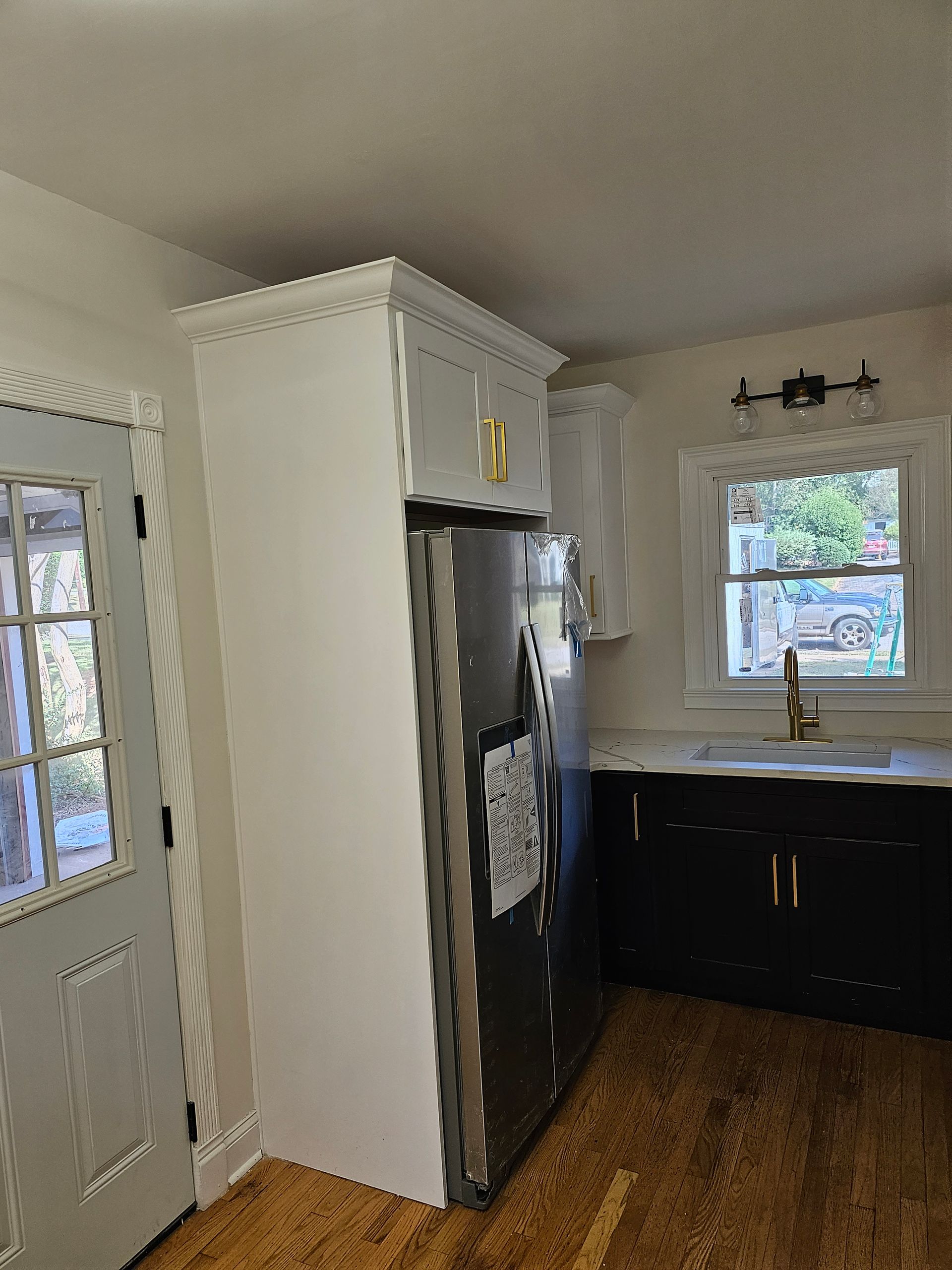 Kitchen with white cabinets, black countertop, gold hardware. Refrigerator, window, and door visible.