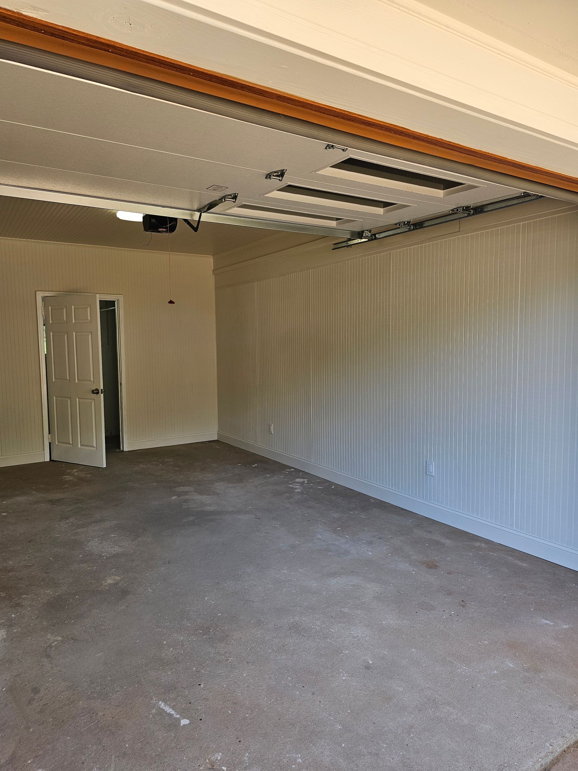 Empty garage with open door, light-colored walls and ceiling, and a concrete floor.
