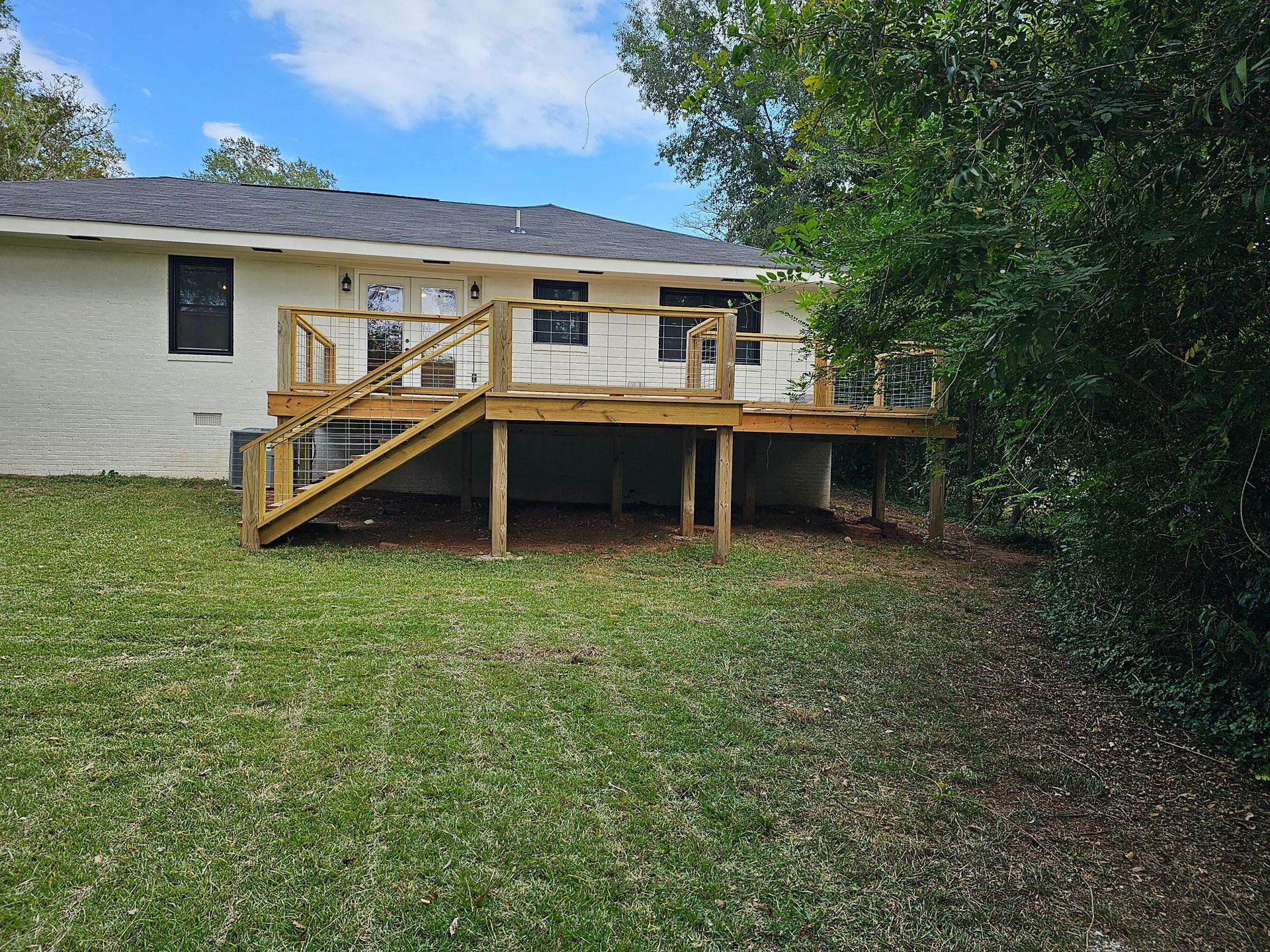 Back view of a white house with a new wooden deck and stairs, set in a grassy yard.