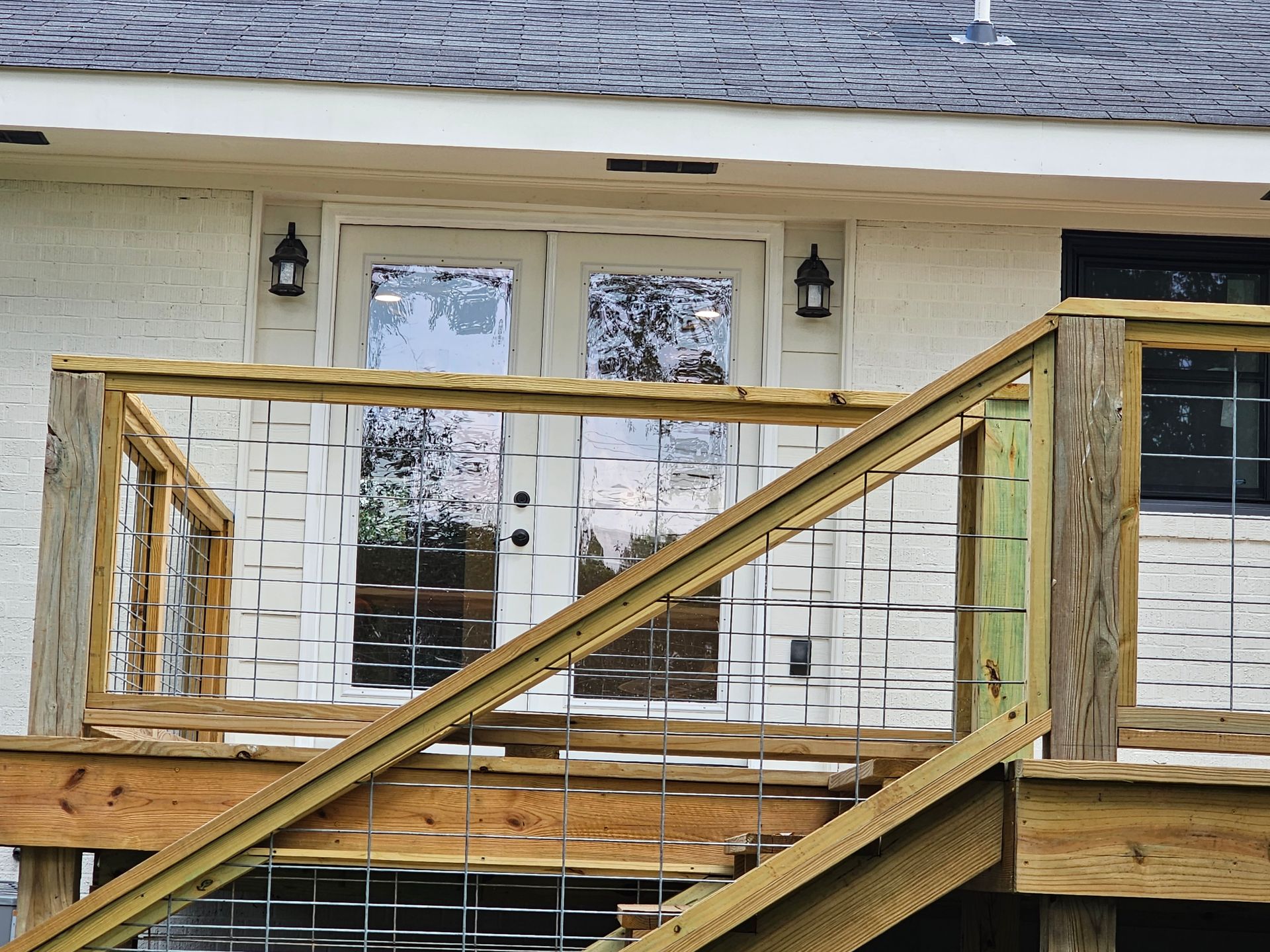 Wooden deck with wire railings, leading to white double doors, and a window.