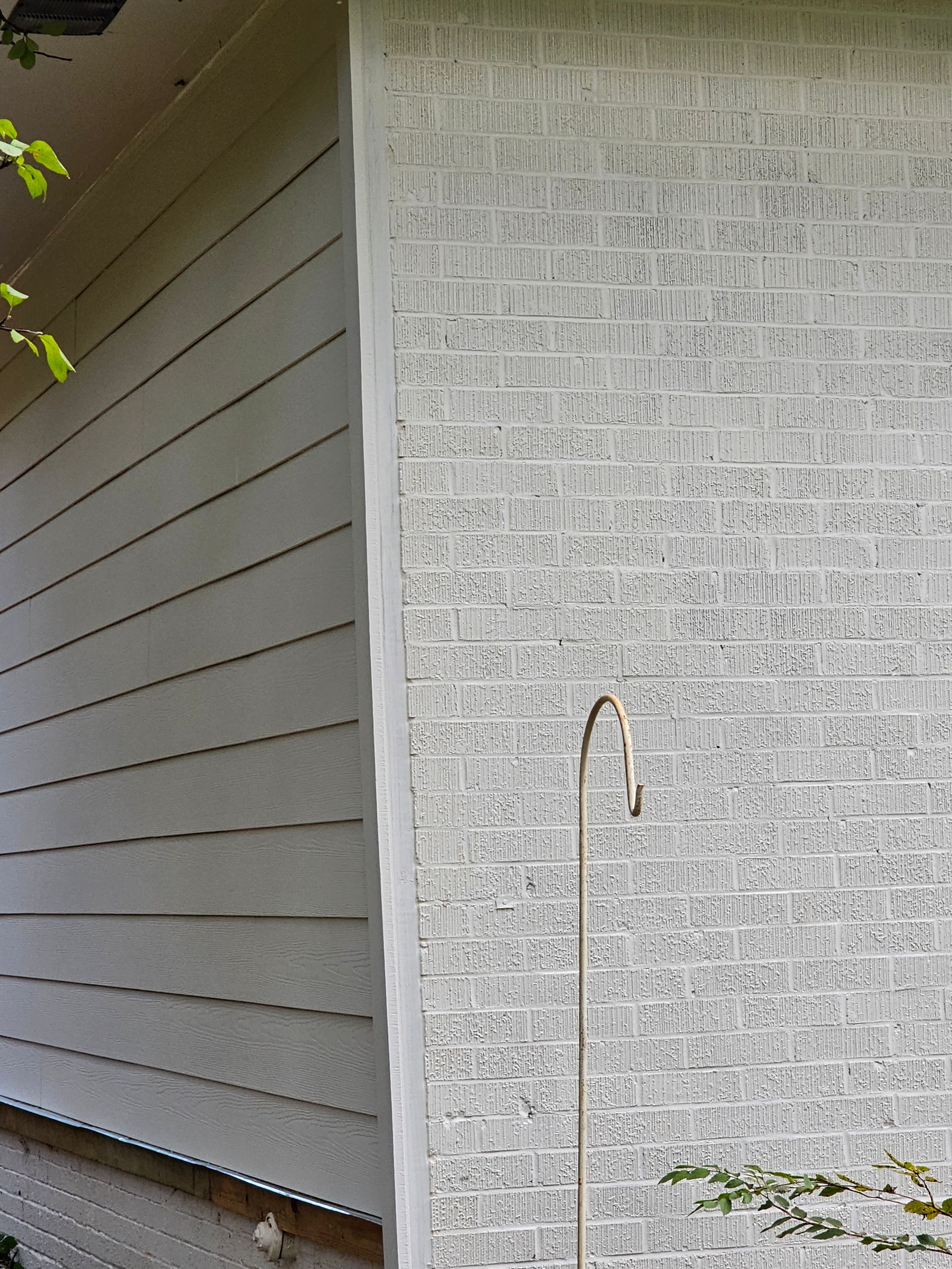 Side of a house, brick wall next to siding. A metal hook pole is in front of the brick.