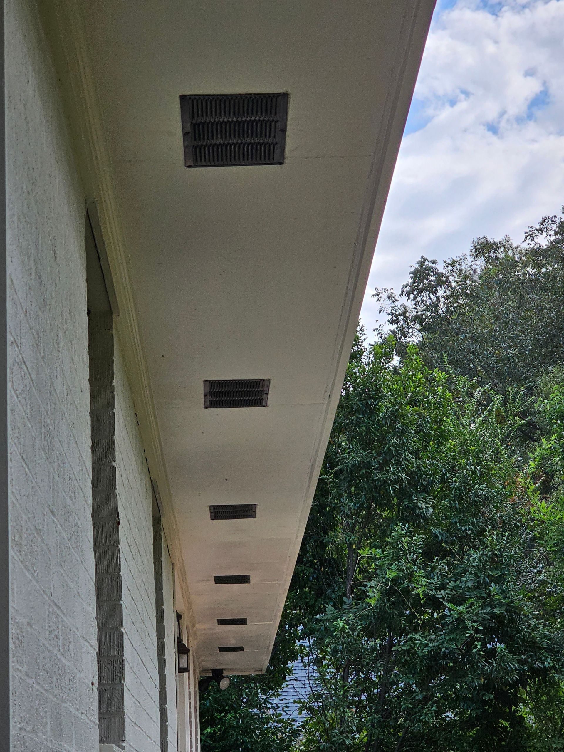 Exterior view of a building with a row of vents along the roofline. Green trees in the background.