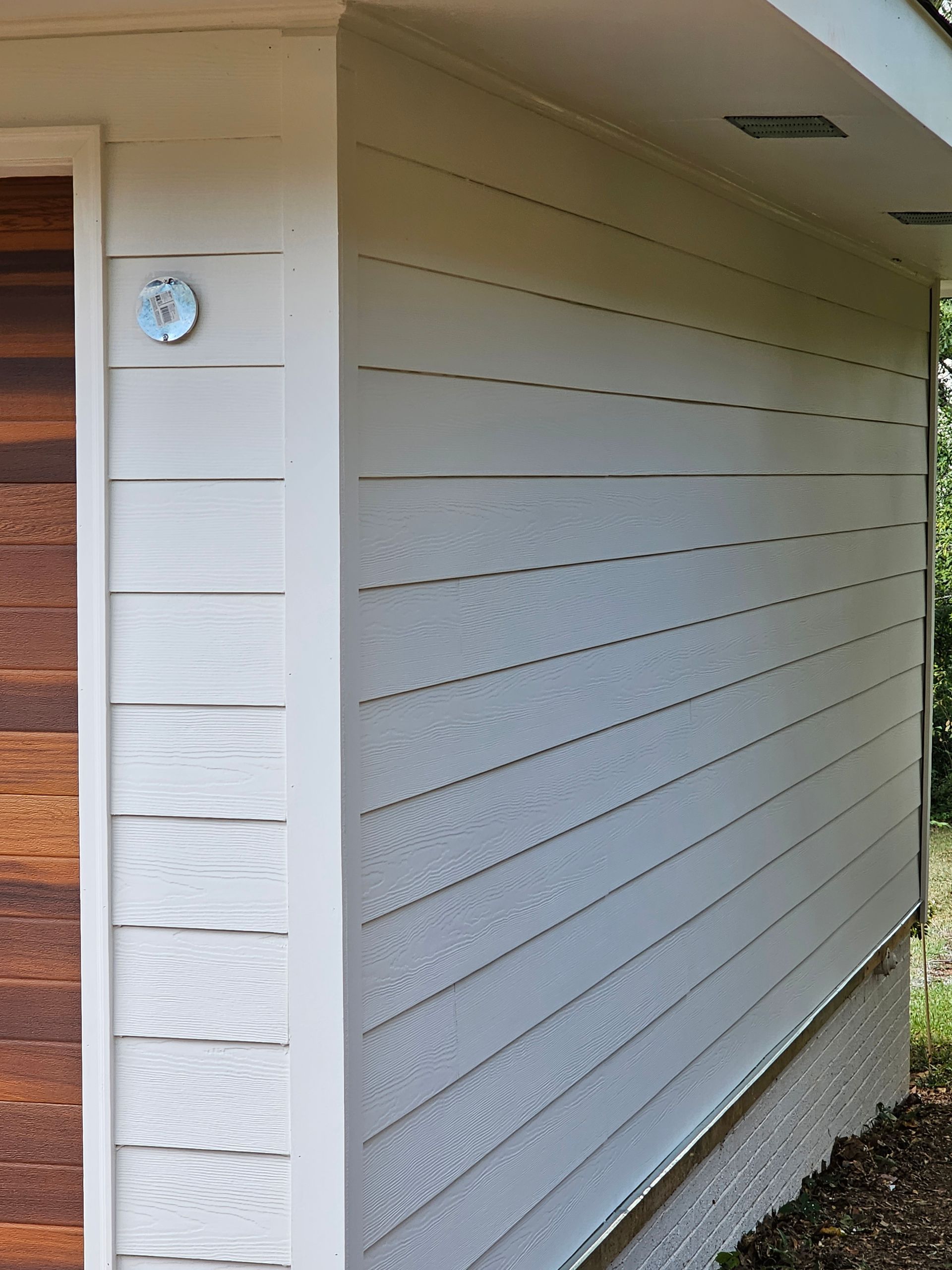 Exterior of a building with white horizontal siding and a brown wooden door.
