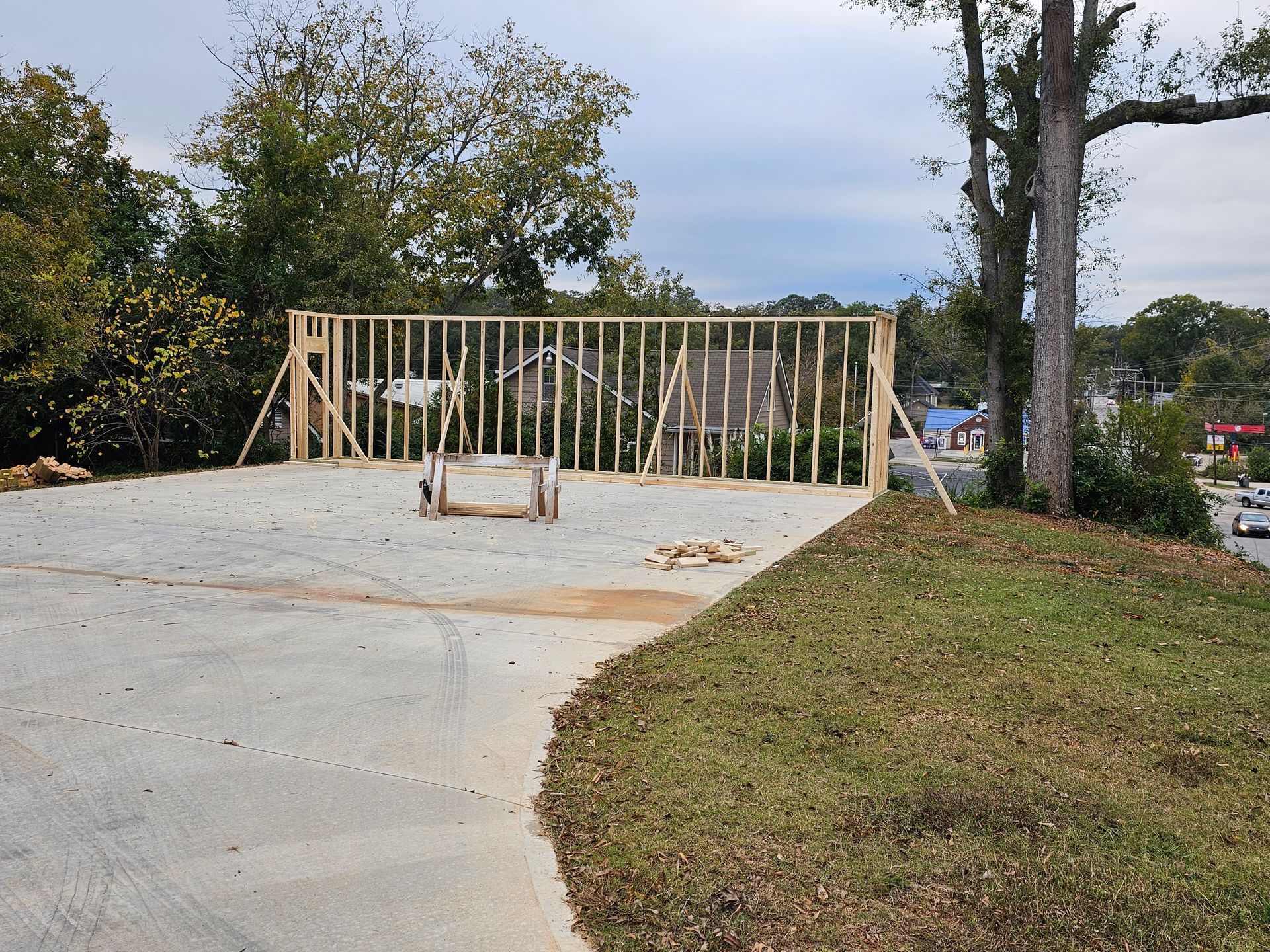 Wooden framework construction on a concrete pad, with a grassy area in the foreground and trees in the background.