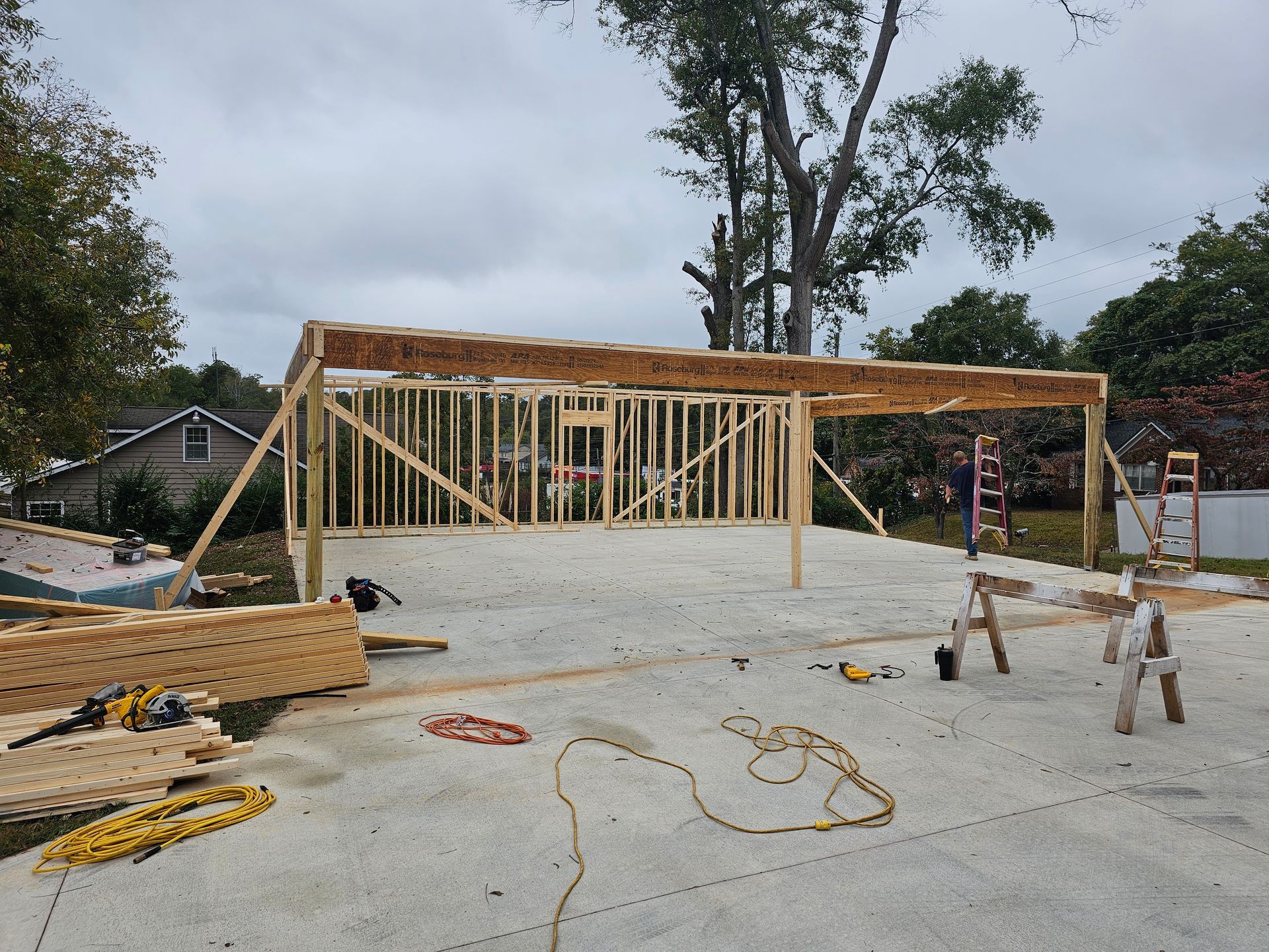 Wood frame structure under construction on a concrete pad; materials, tools are present.