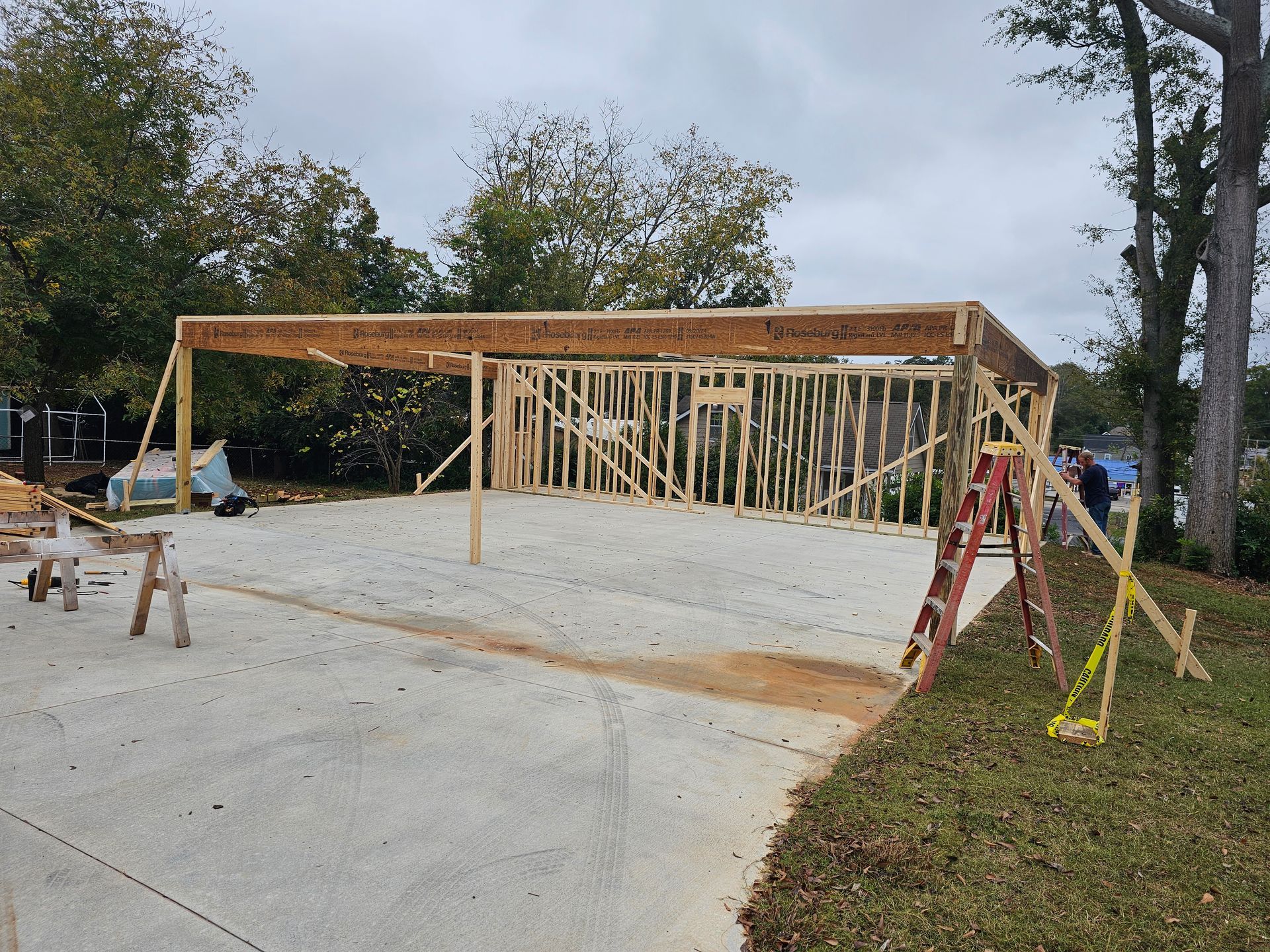 Wood frame of a carport under construction on a concrete driveway, with a ladder and tools present.