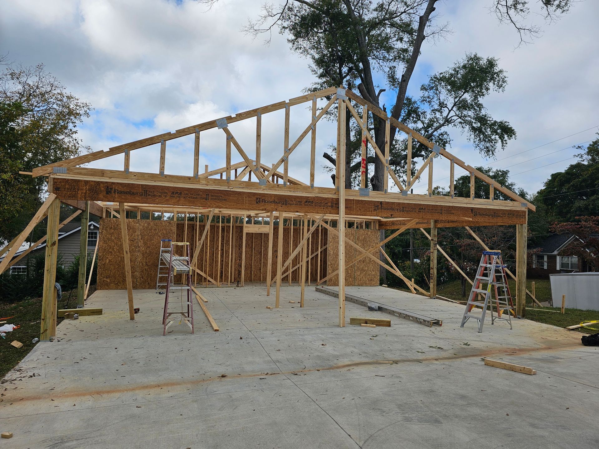 Garage under construction: wooden frame with a concrete foundation, cloudy sky.