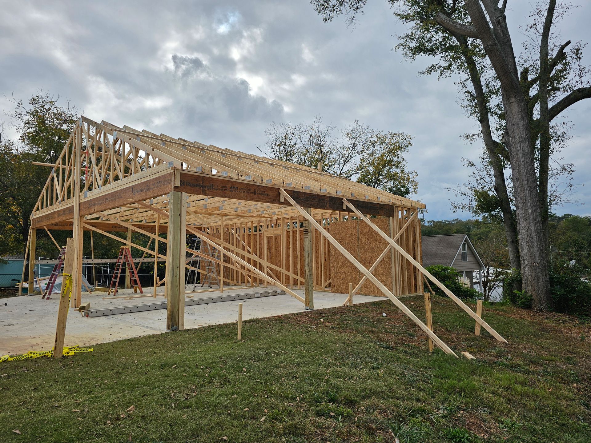 Wooden structure of a building under construction on a concrete base, supported by braces, outdoors.