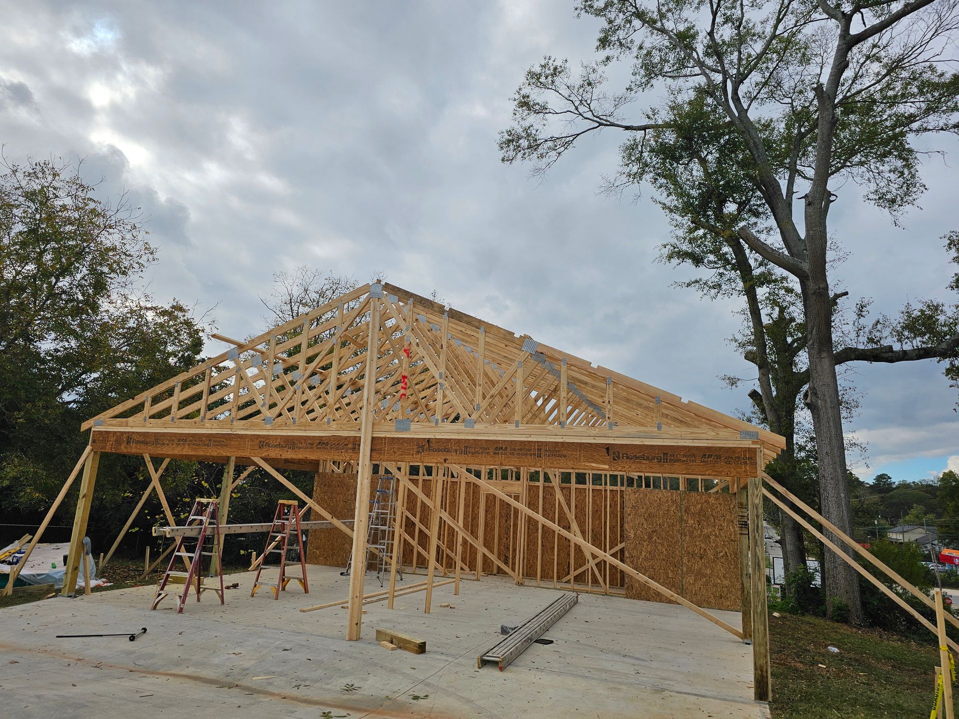 Wood framing for a building with a gabled roof under construction on a concrete pad.