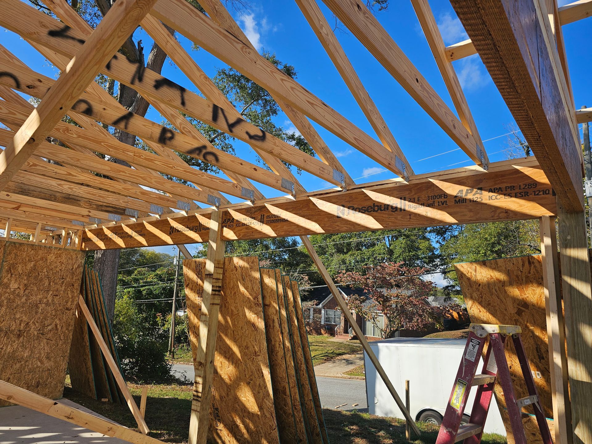 Wooden frame construction of a building with blue sky. OSB walls, roof trusses, and a ladder are visible.