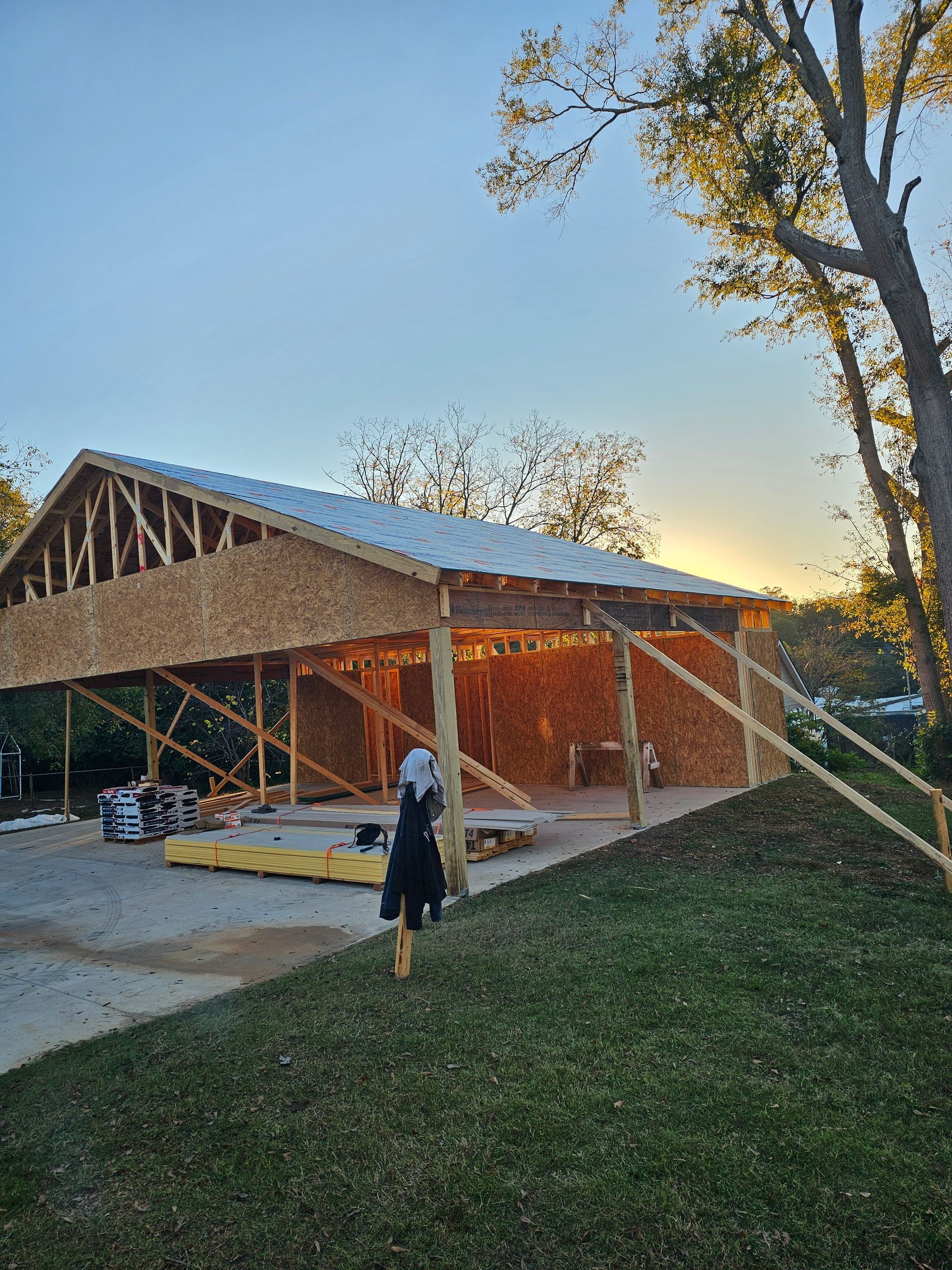 Wooden structure under construction, with a partially built roof, set against a sunset sky.