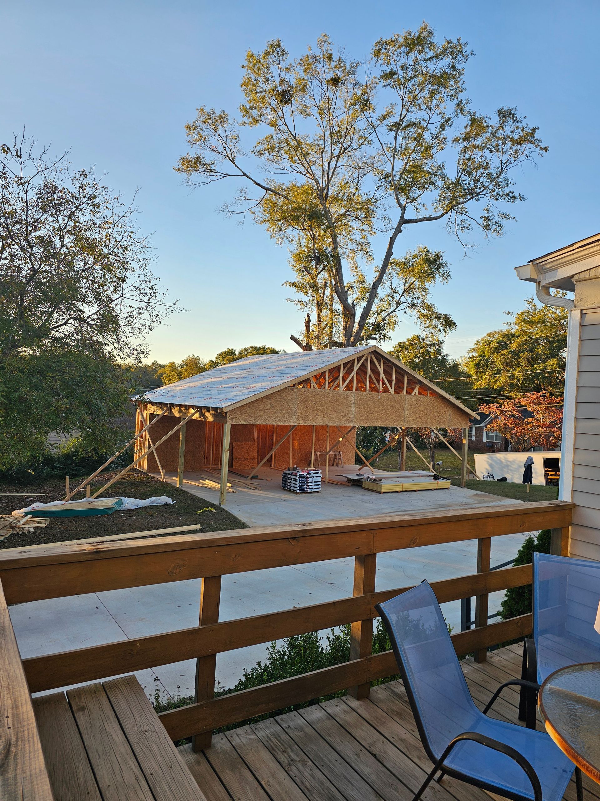 Construction of a garage with exposed wooden framing and a concrete foundation, viewed from a wooden deck.