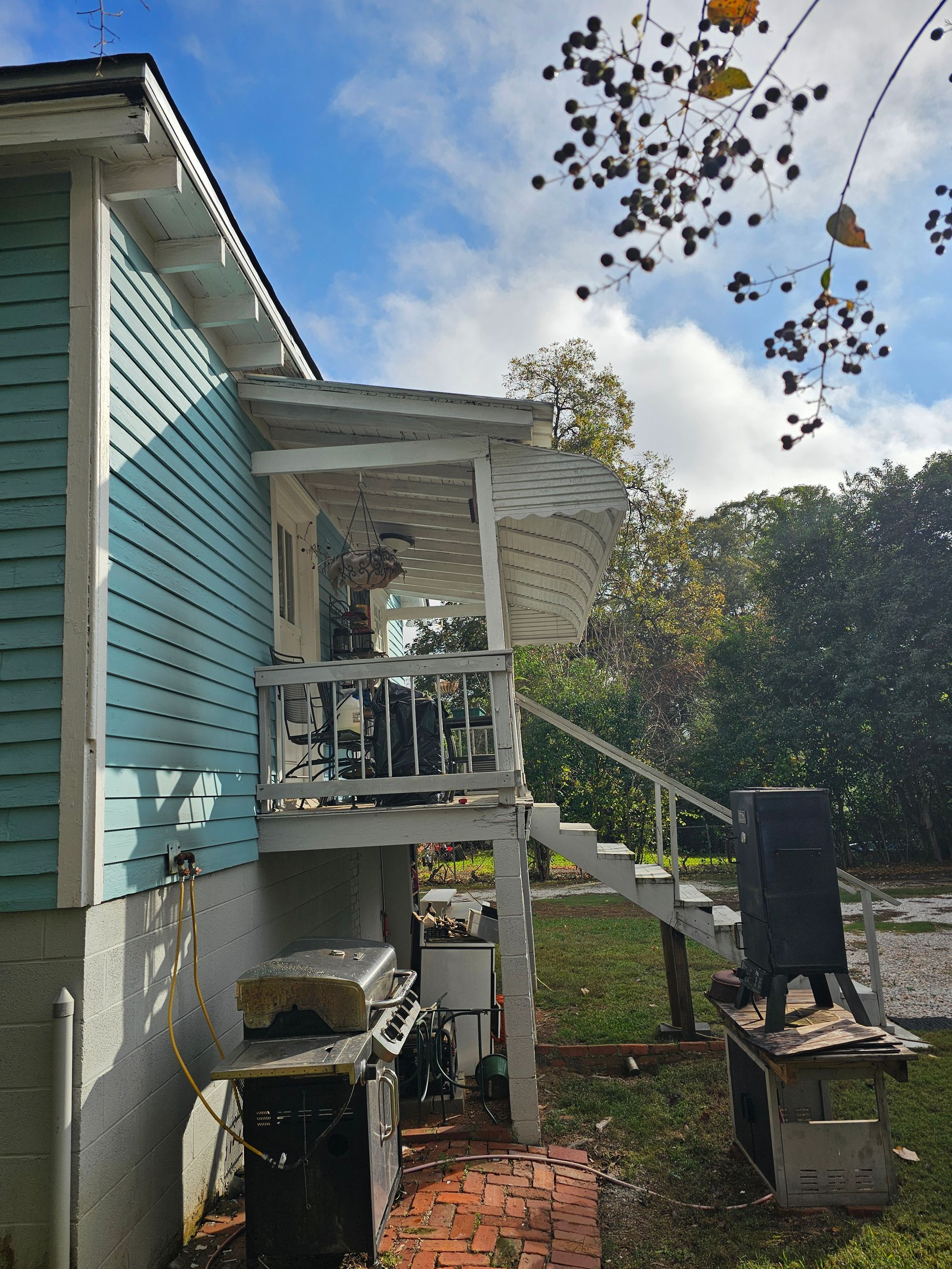 Side of a house with a porch and stairs. The house is light blue with white trim. A grill is visible underneath the porch.