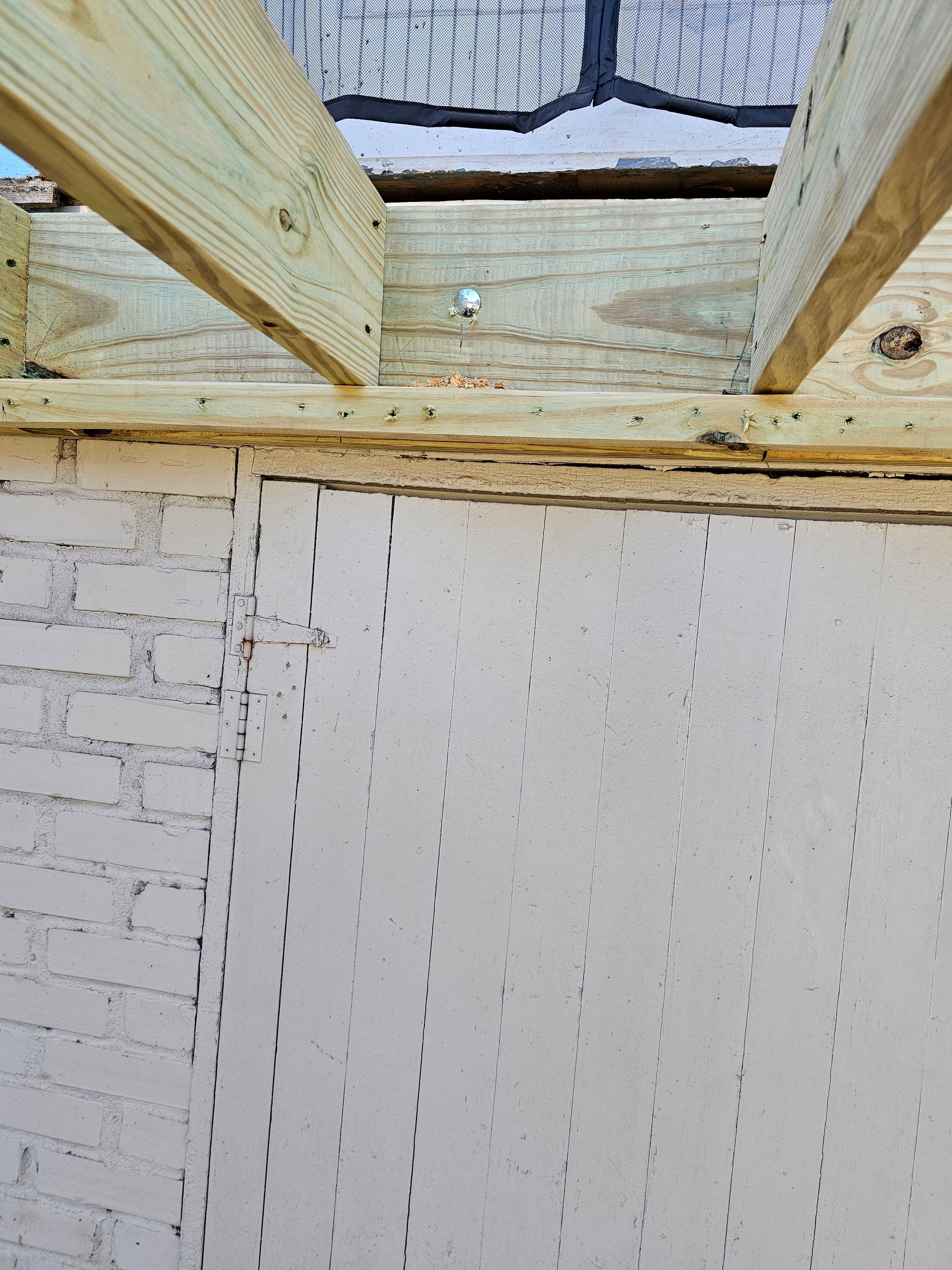 View of wooden beams and white siding. The beams are supporting a roof. The siding is vertical and appears new.