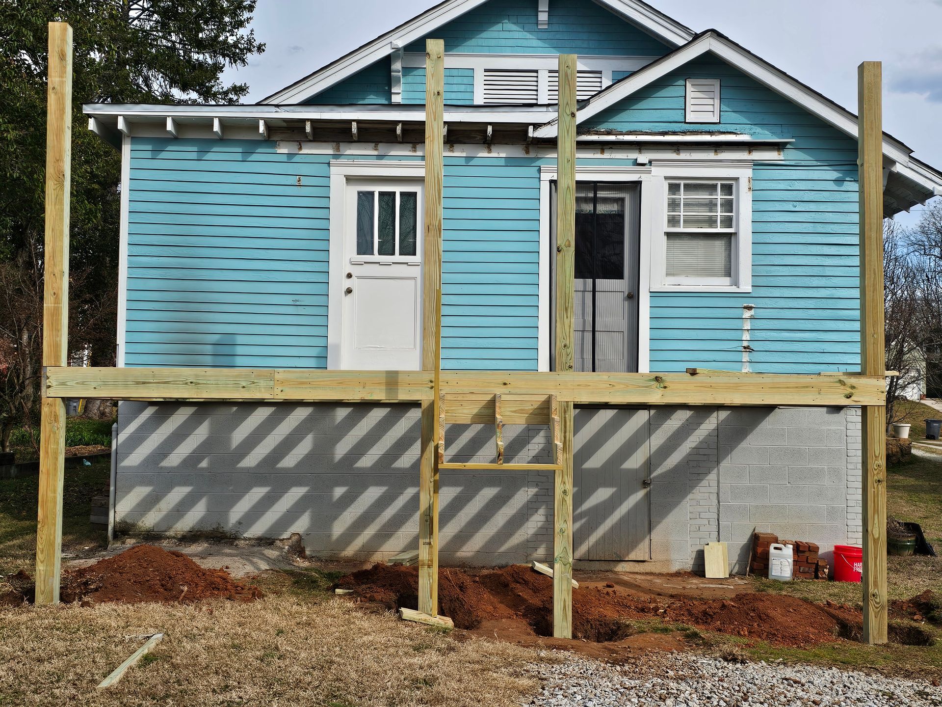 A partially built wooden deck in front of a blue house with a white door and window.