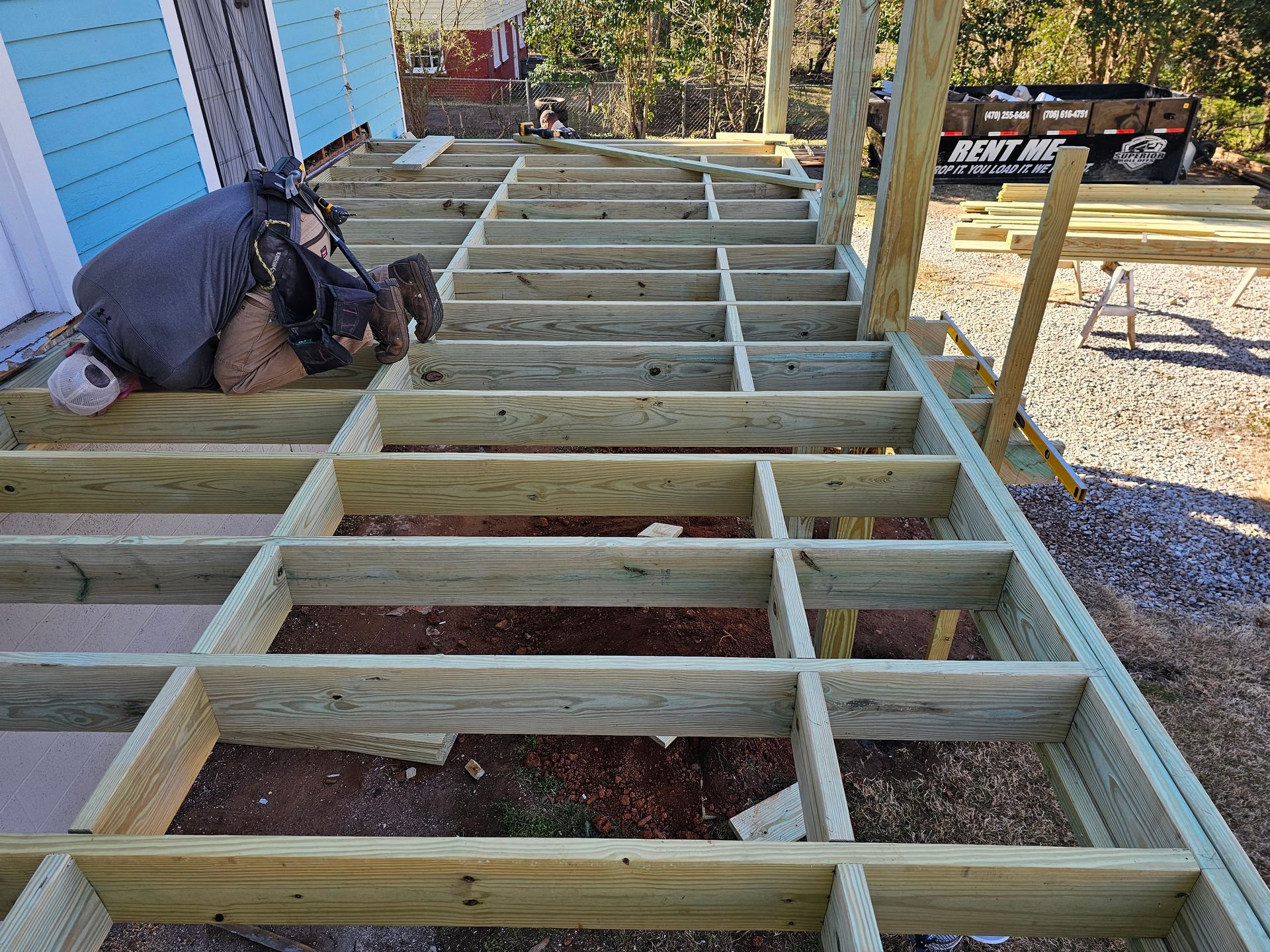 Construction worker installing deck frame outdoors. Wooden beams, sunny day.