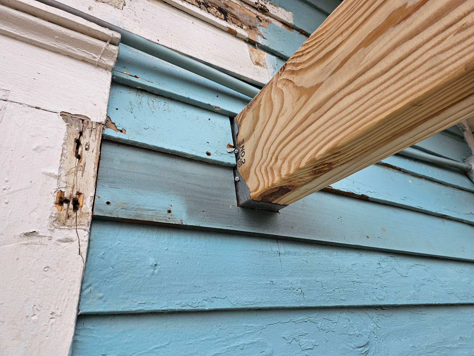 Wooden beam supported by metal bracket attached to blue siding.