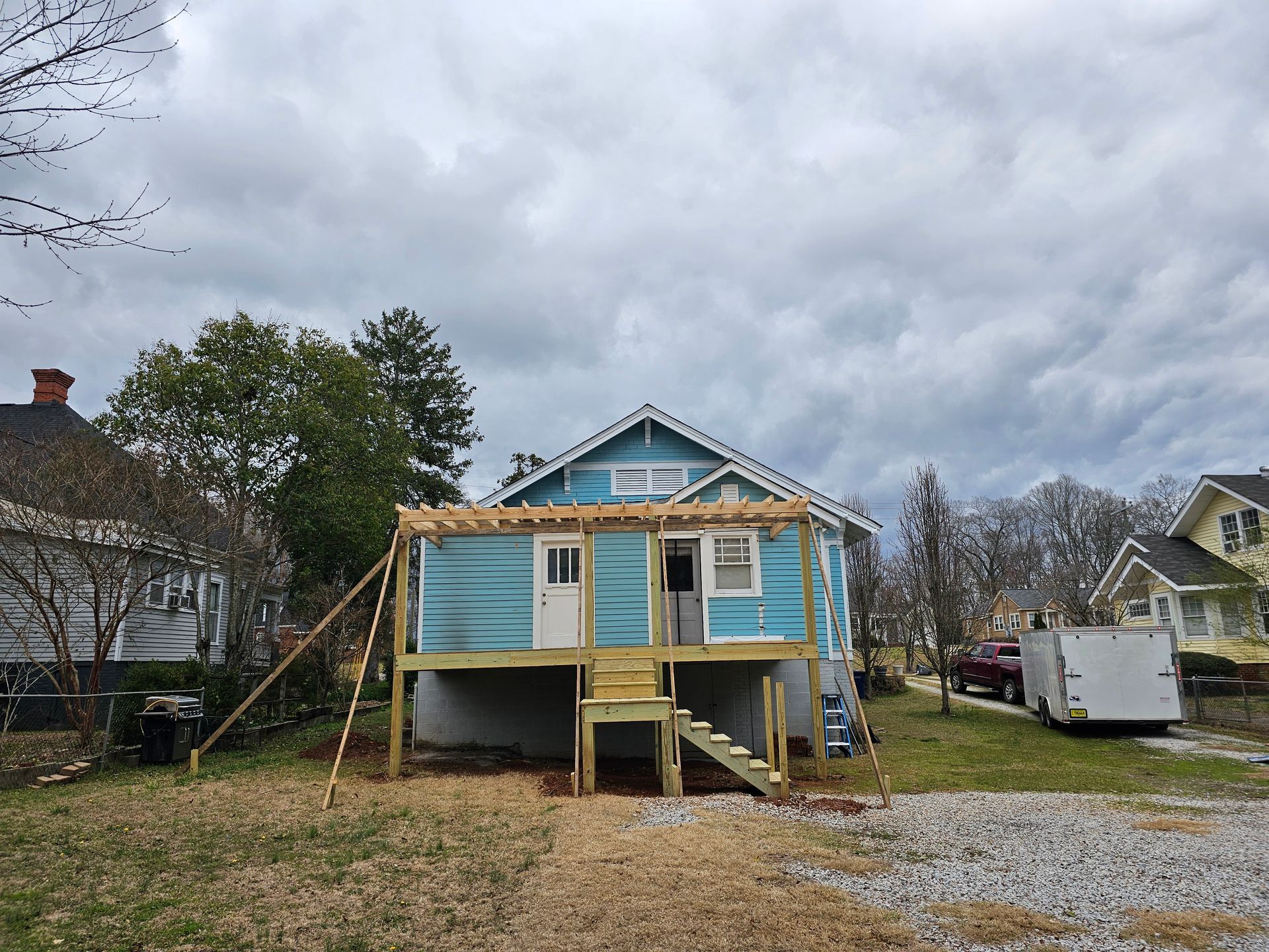 Blue house with new wooden deck construction, stairs, and cloudy sky.