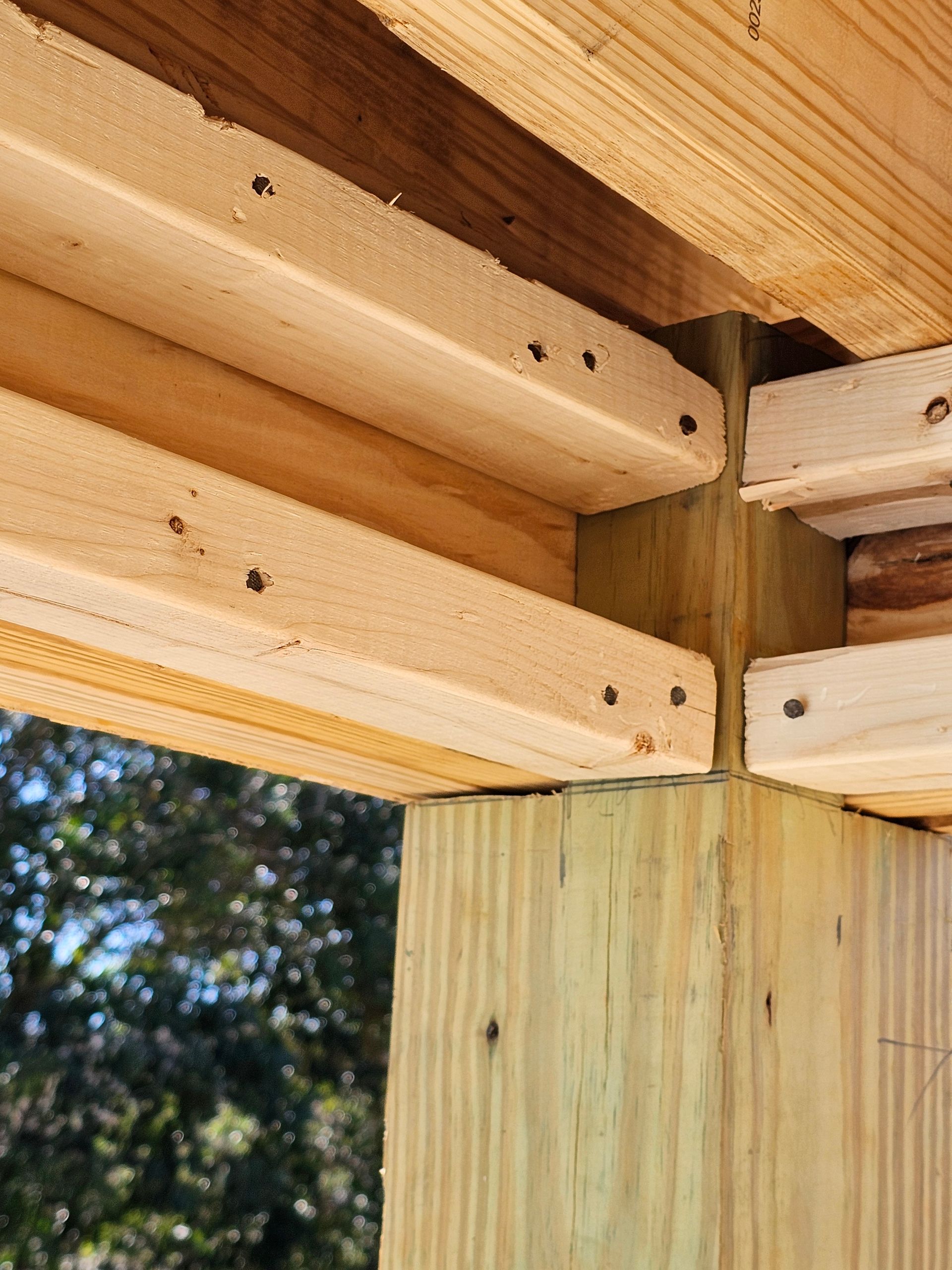 Wooden beams joined at a corner post, construction detail.  Visible nails securing the boards.