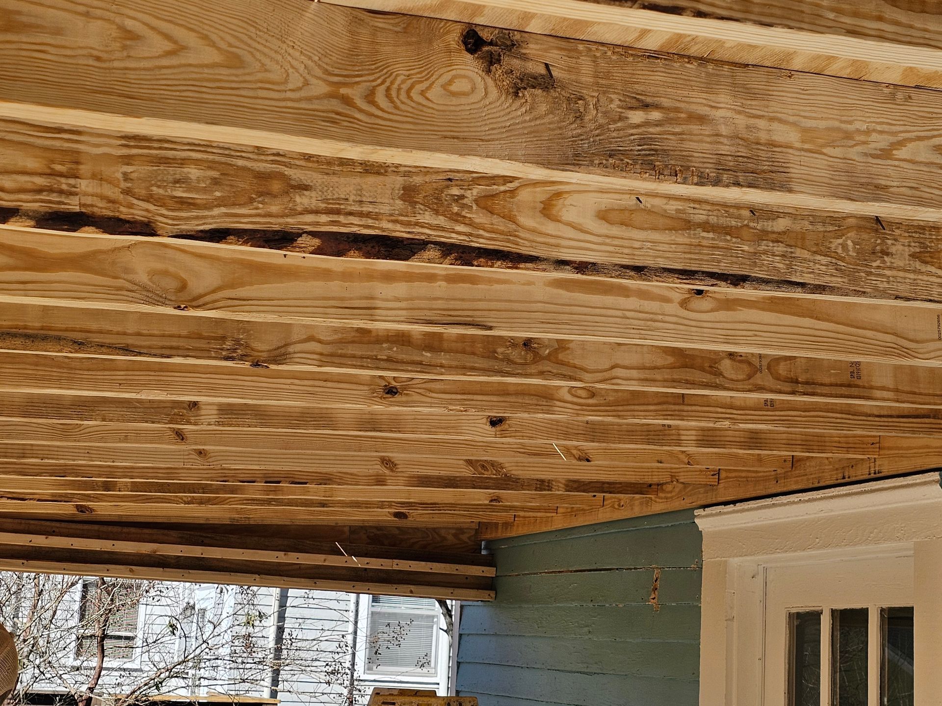 Wooden porch ceiling, visible boards. Blue wall and a white door frame visible below.