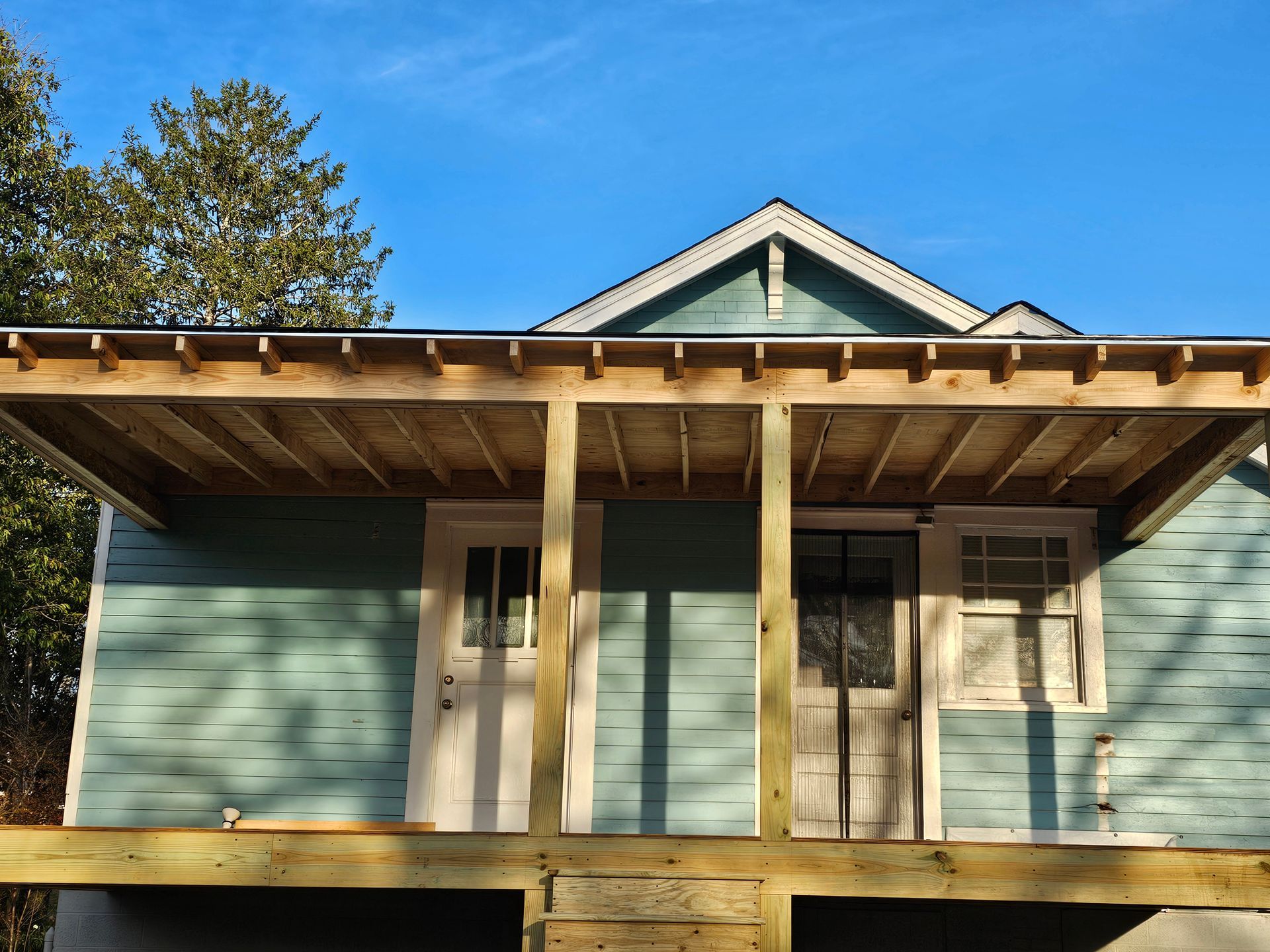 Blue house with a wooden porch and roof, two doors, and a clear blue sky.