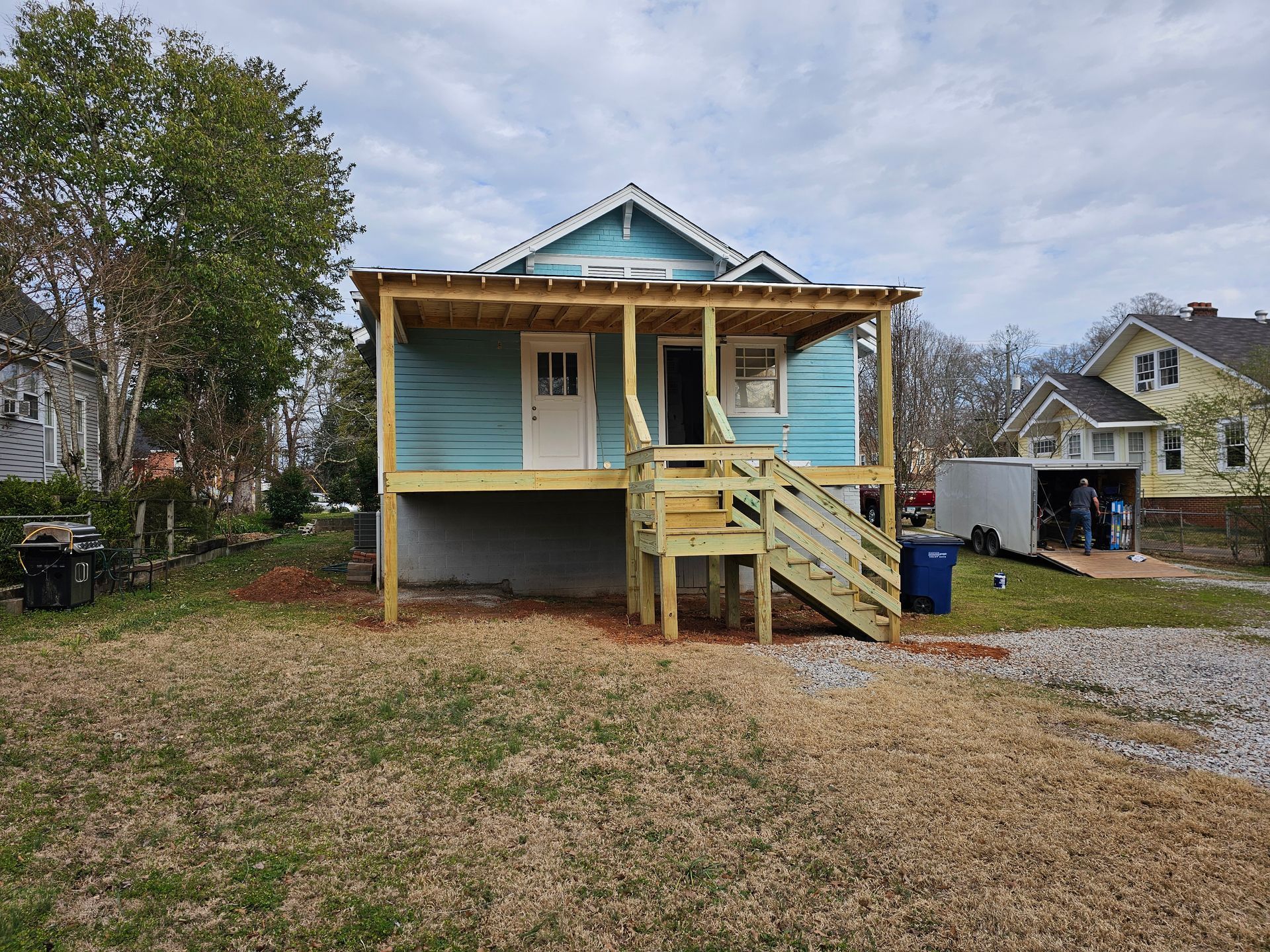 Blue house with a newly built wooden porch and stairs, in a grassy yard under a cloudy sky.