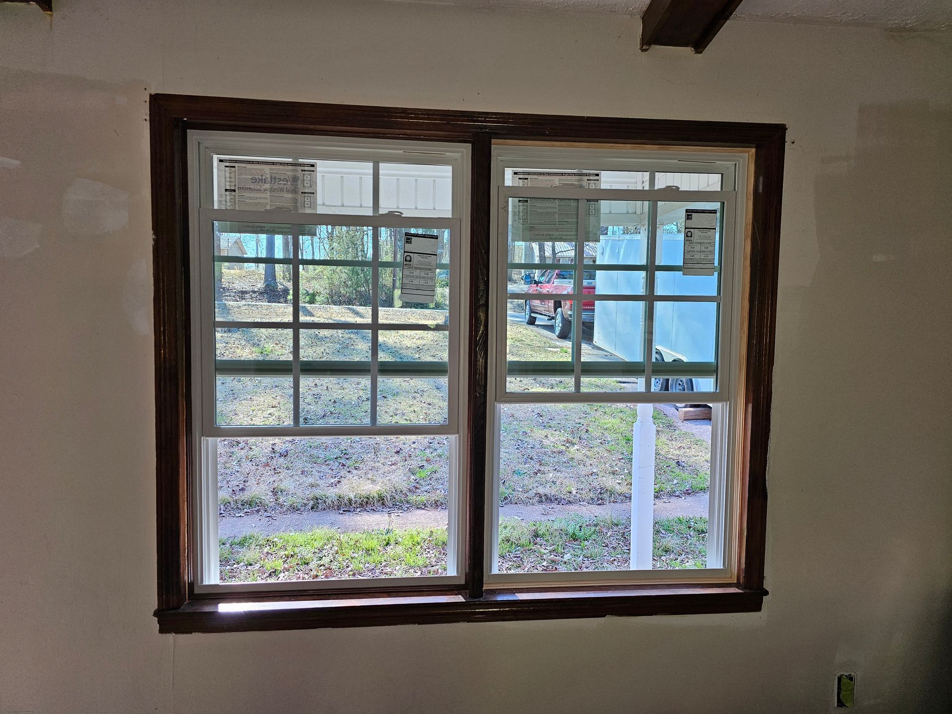 Two-pane window with dark wood trim, showing a view of the outdoors: grass, trees, and a vehicle.