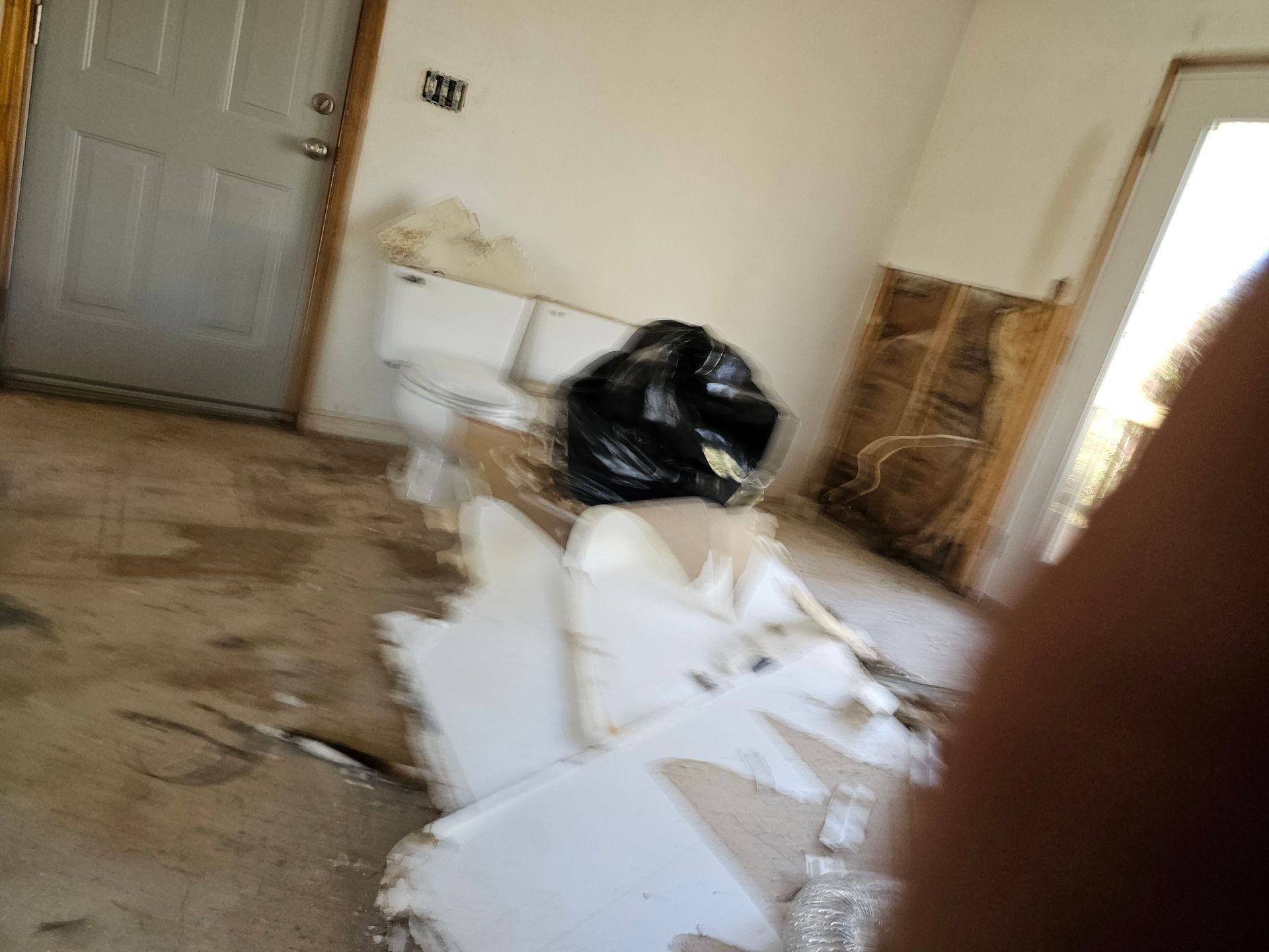 Room with debris and damage, including a black trash bag and exposed wall. Door on left.