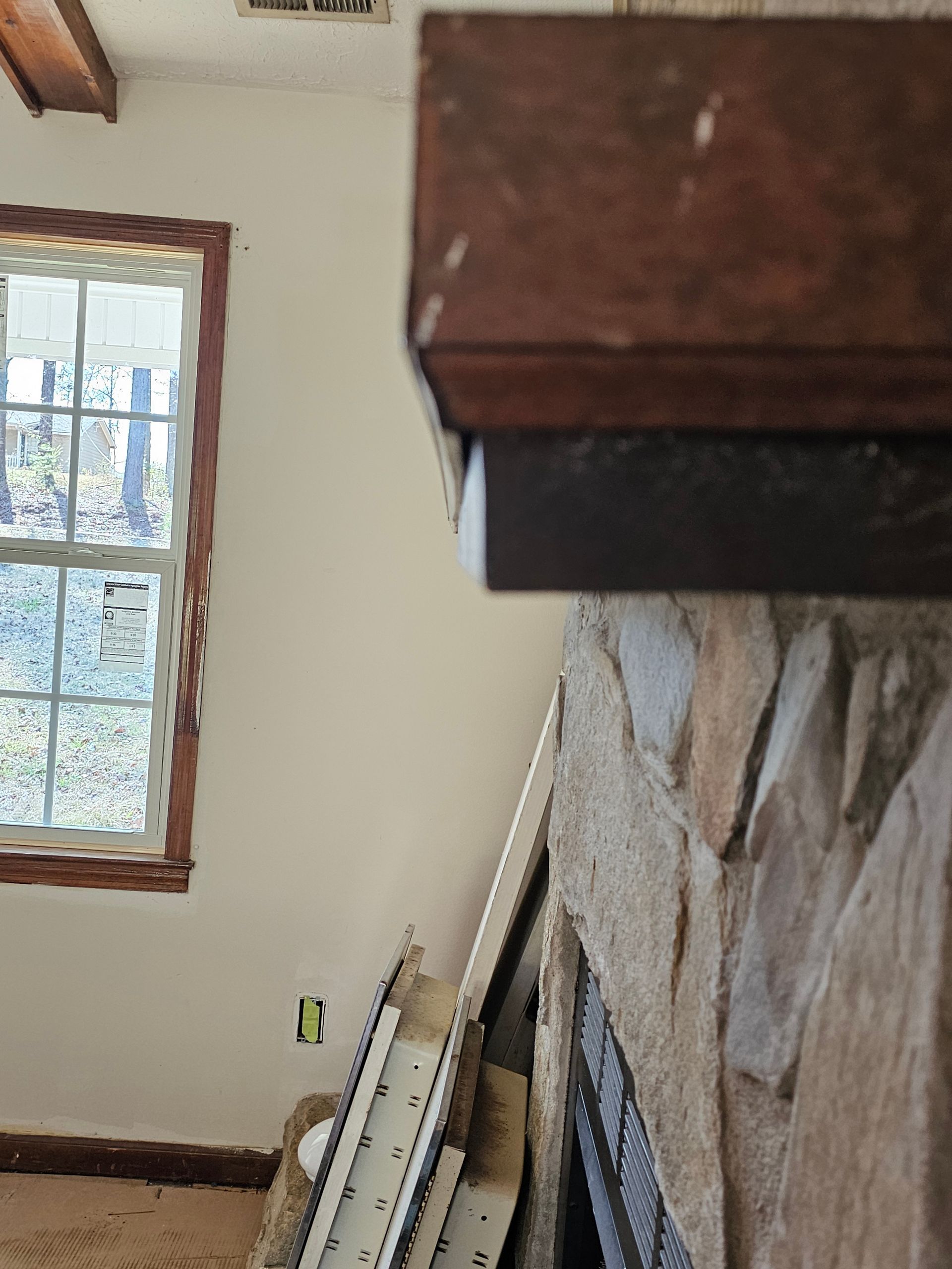 Interior view of a room with a stone fireplace, window, and wood mantel. Construction materials lay in front.