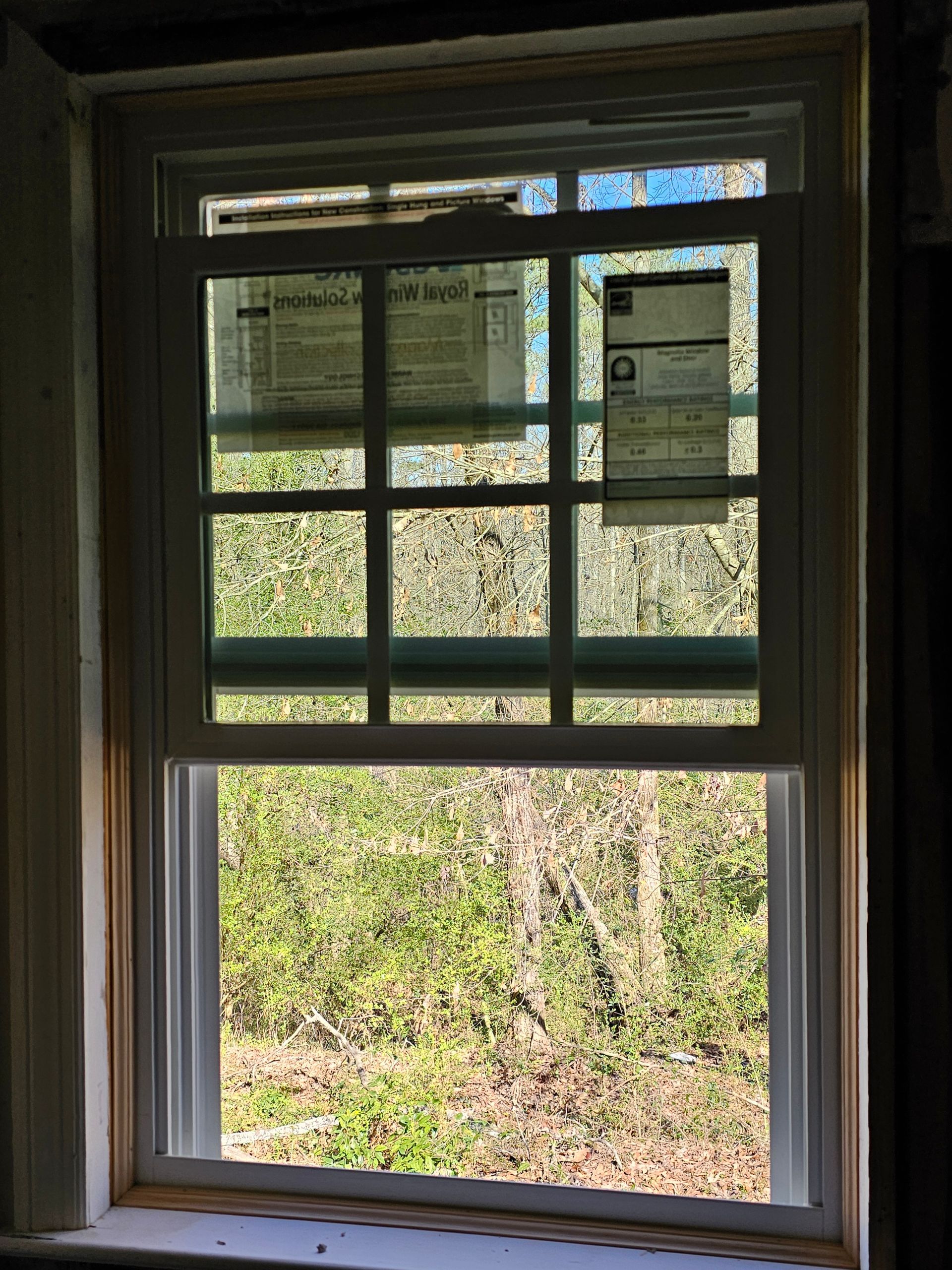 New double-hung window with a grid pattern, installed in a white frame, with outdoors visible through the glass.