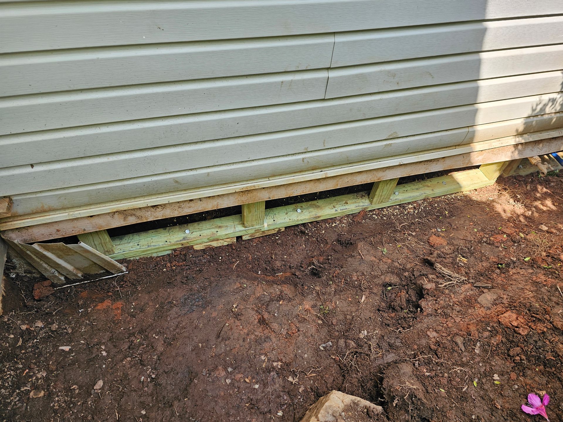 Wooden building foundation with exposed beams above dirt.