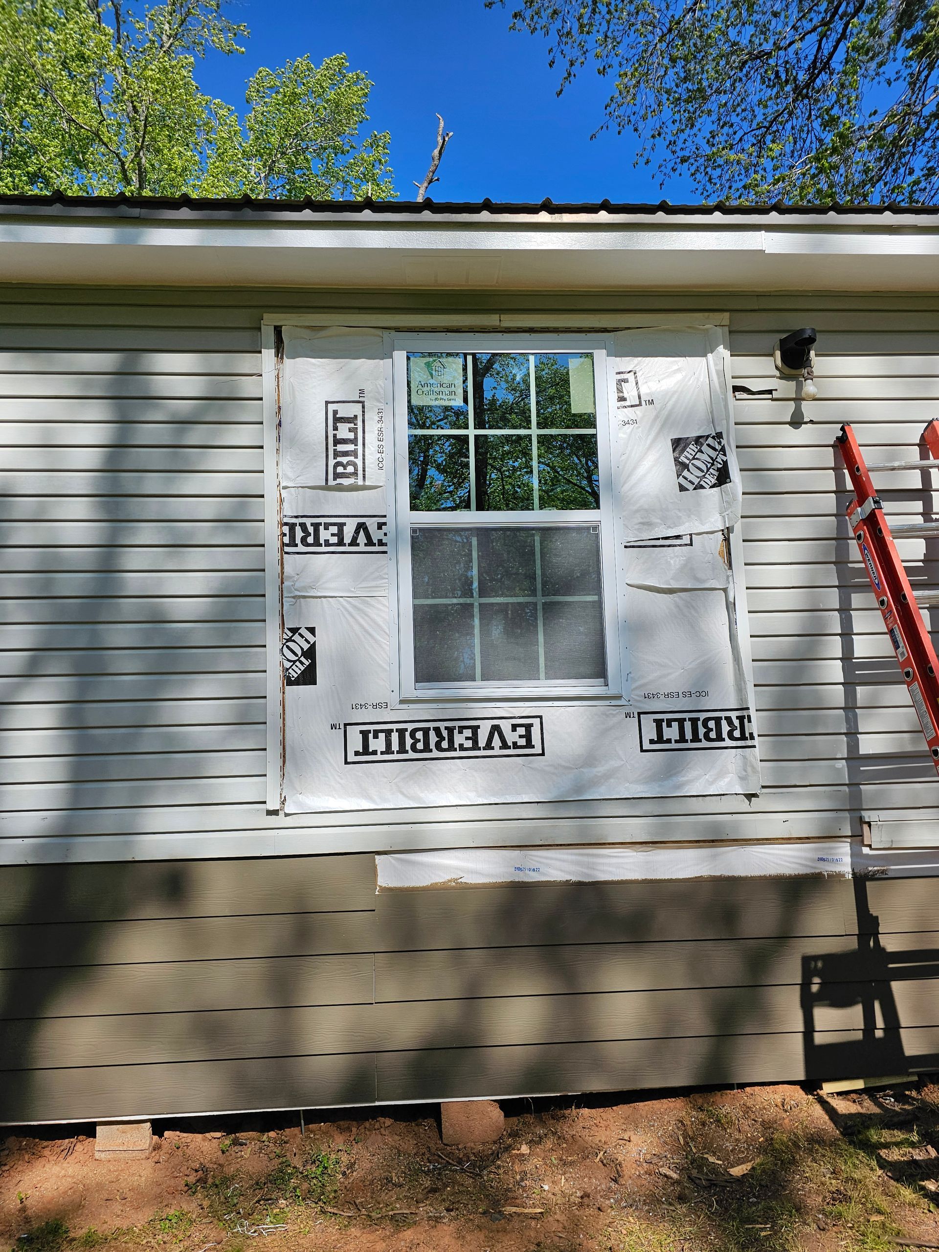 Exterior view of a house with a newly installed window covered with white and black weather-resistant barrier.