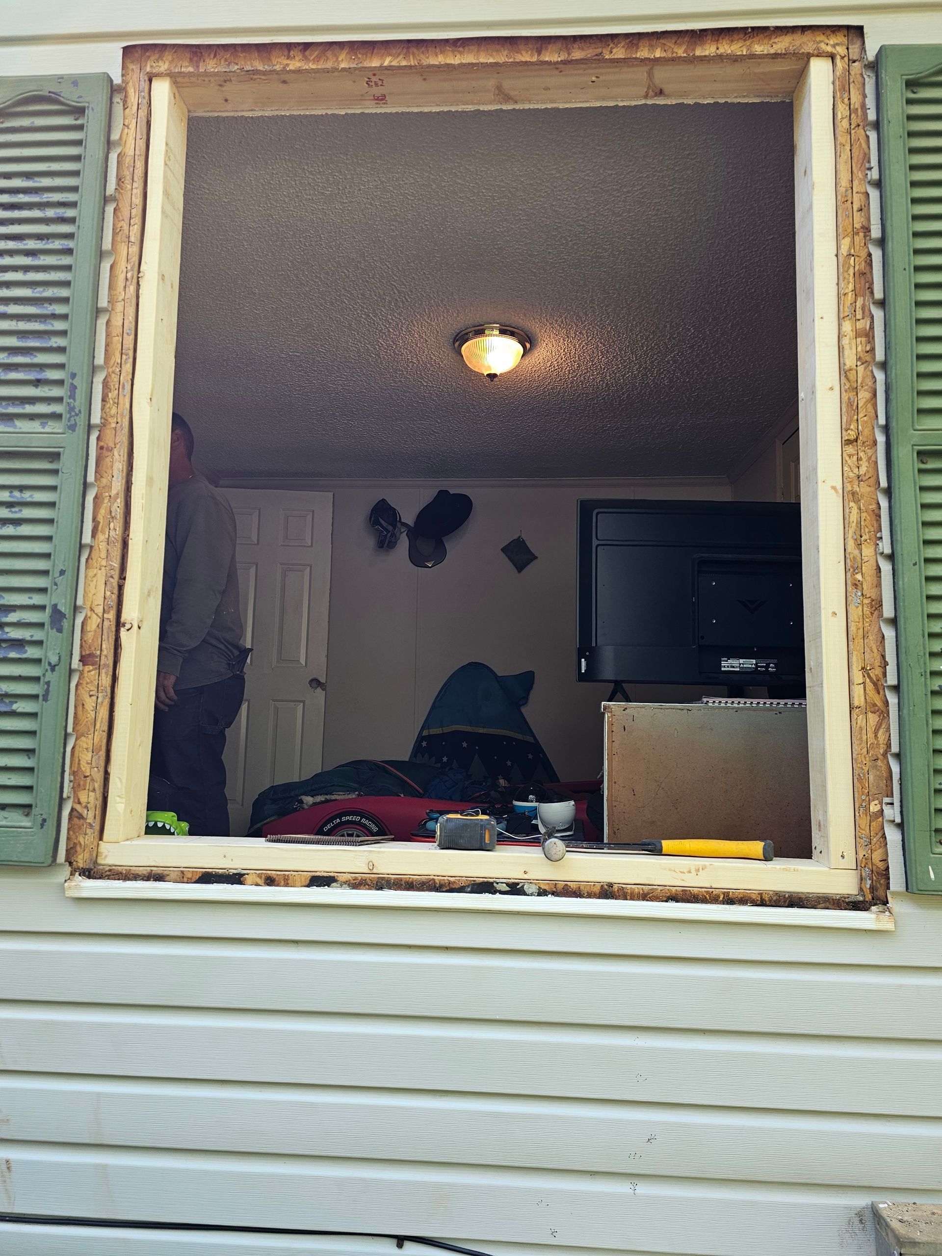 Open window frame looking into a room with a person, TV, and ceiling light.
