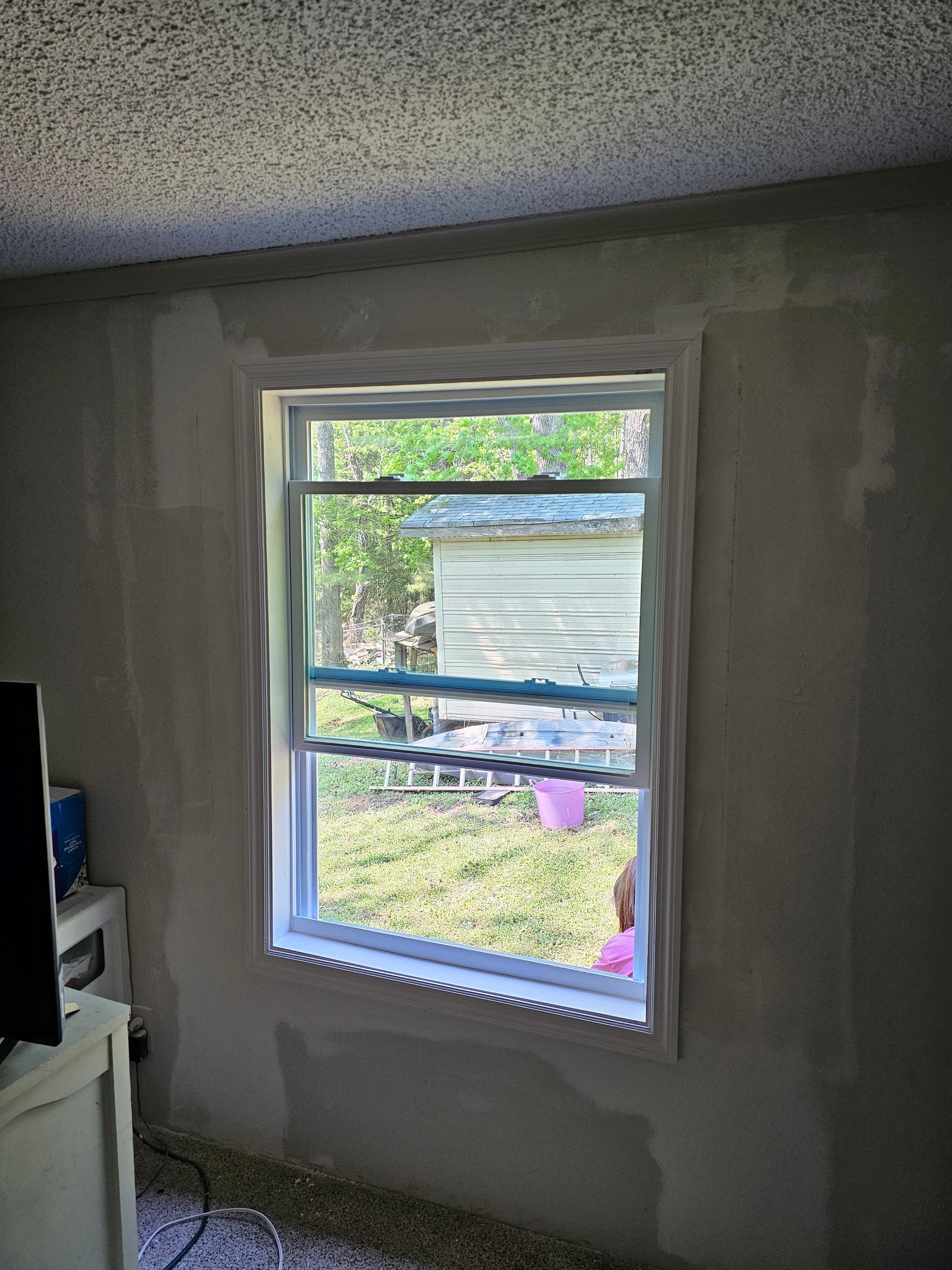 Window with white trim and view of a yard. Patchwork wall surrounds the window.