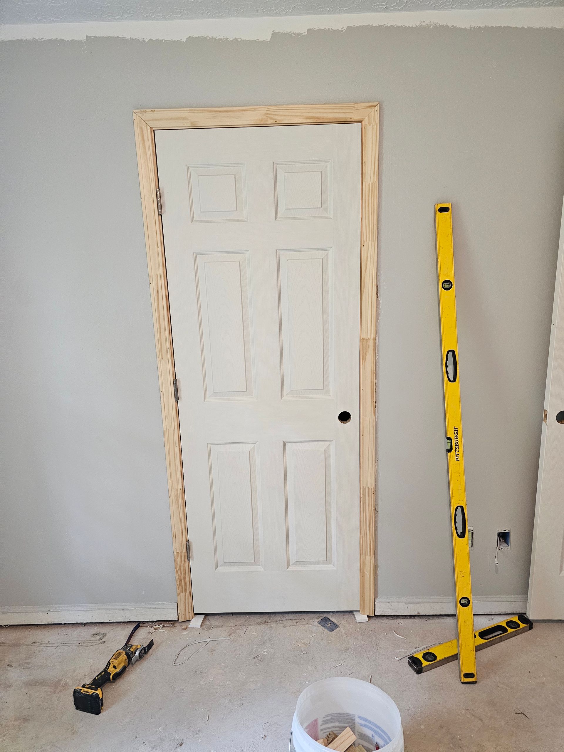 Door installation in progress; white door in a gray-walled room. A level and tools are nearby.