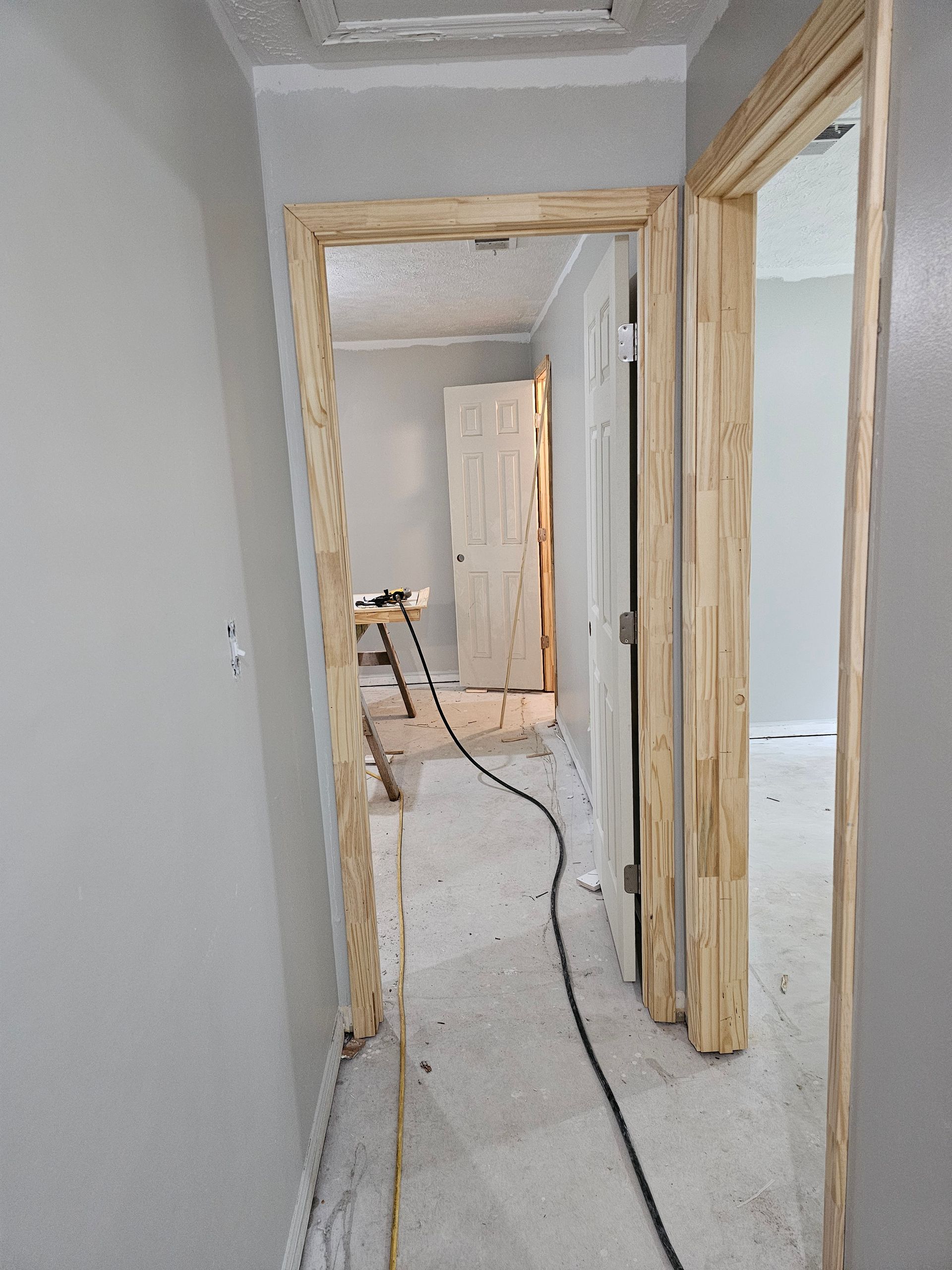 Hallway with unfinished door frames. A doorway leads to another room. Gray walls and flooring.