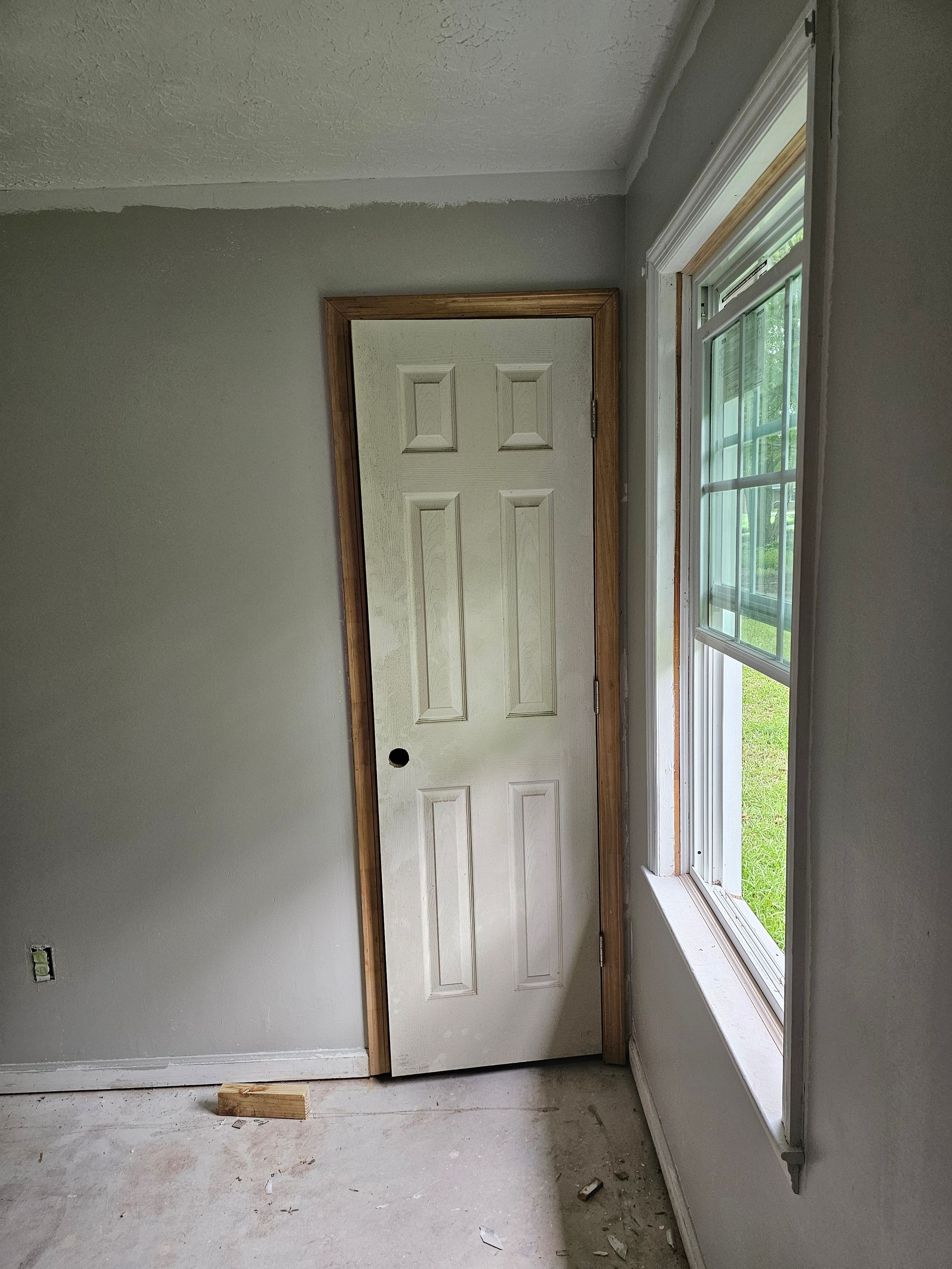 White door, window in corner of a room, gray walls, unfinished construction.