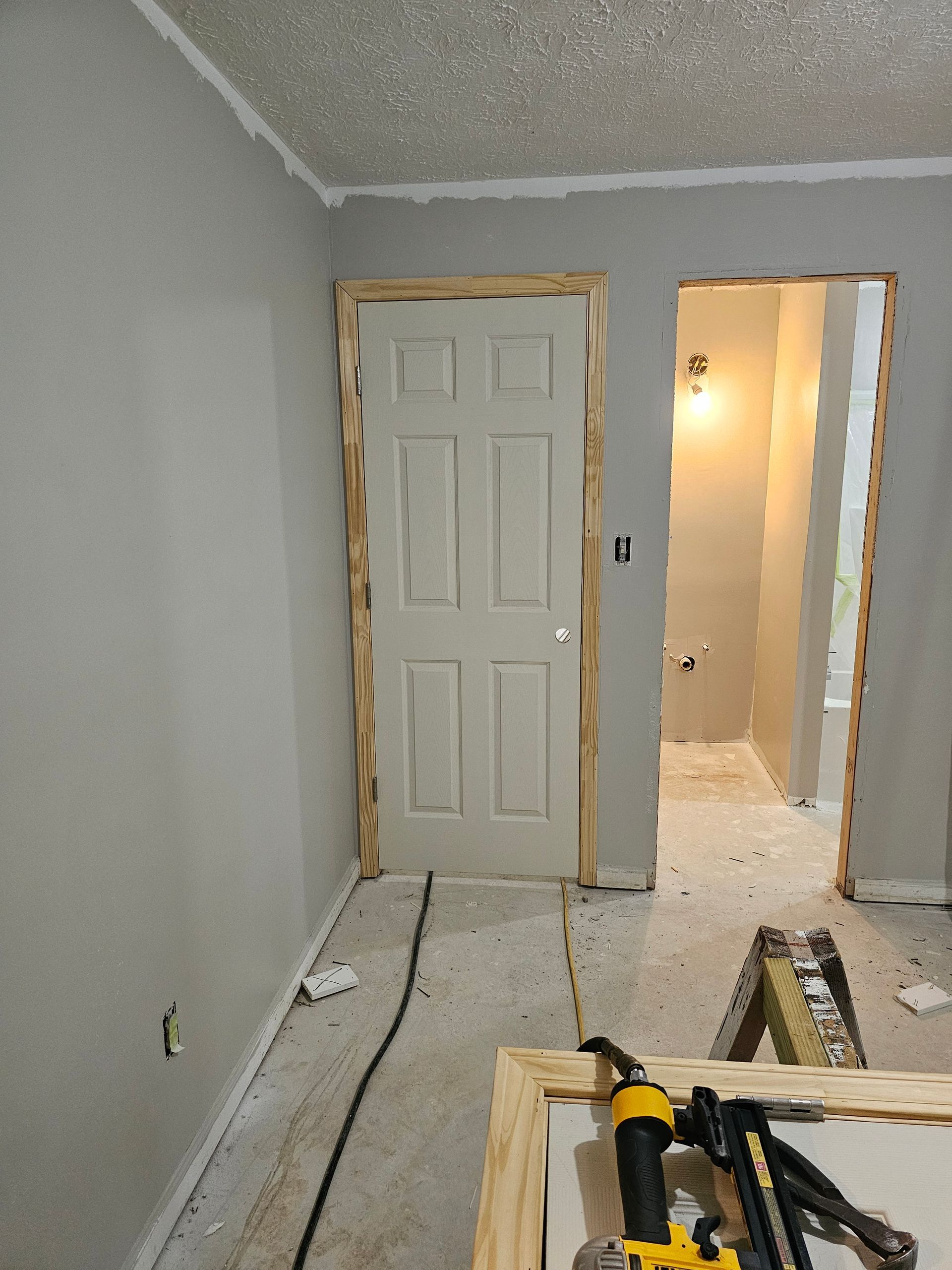 Interior room with unfinished doorway, door, and trim; gray walls, white door, construction tools.