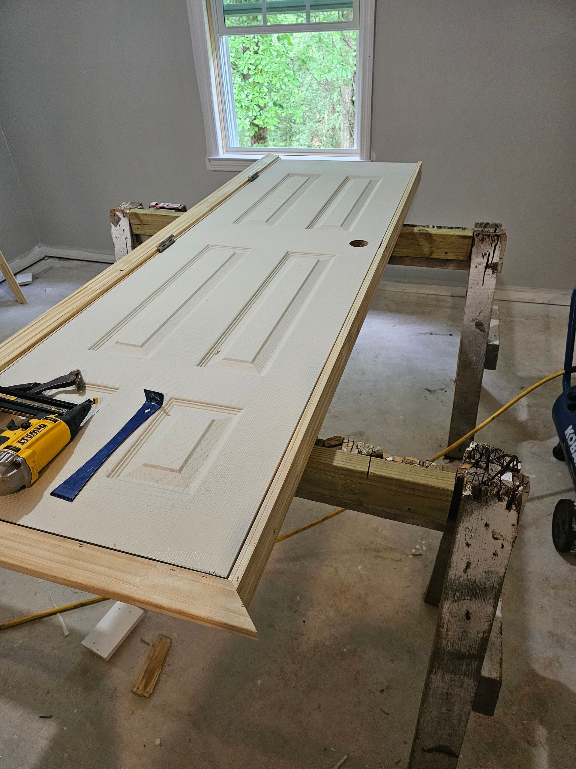 Door laid on sawhorses in room; tools visible. Window in background.