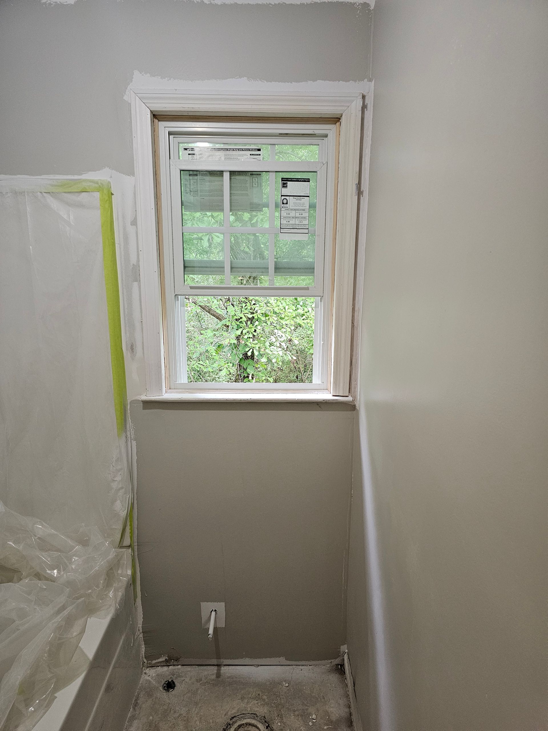 Bathroom window during renovation with neutral wall paint and protective plastic.