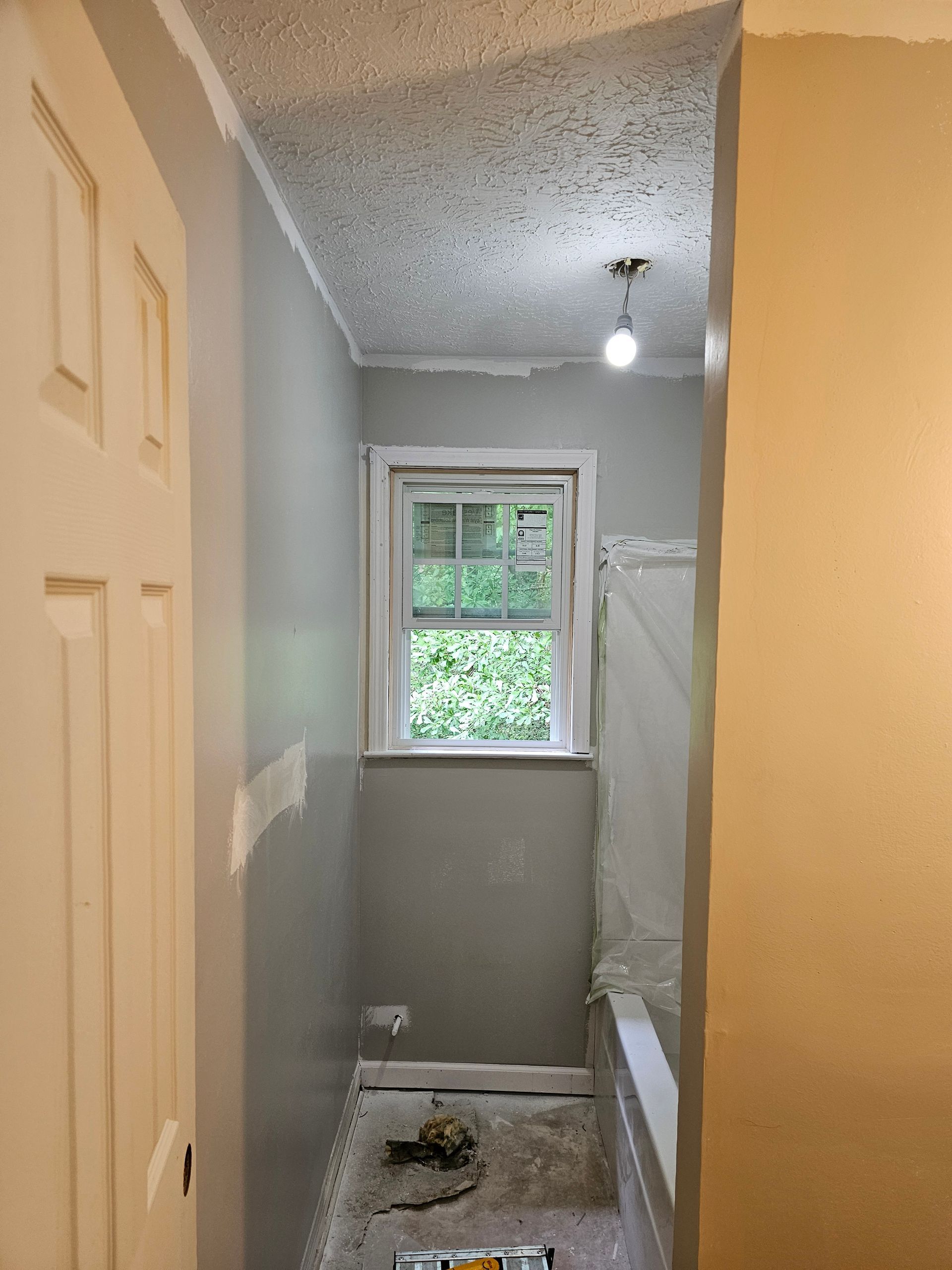 Bathroom interior under construction with a window, white door, and light gray walls.