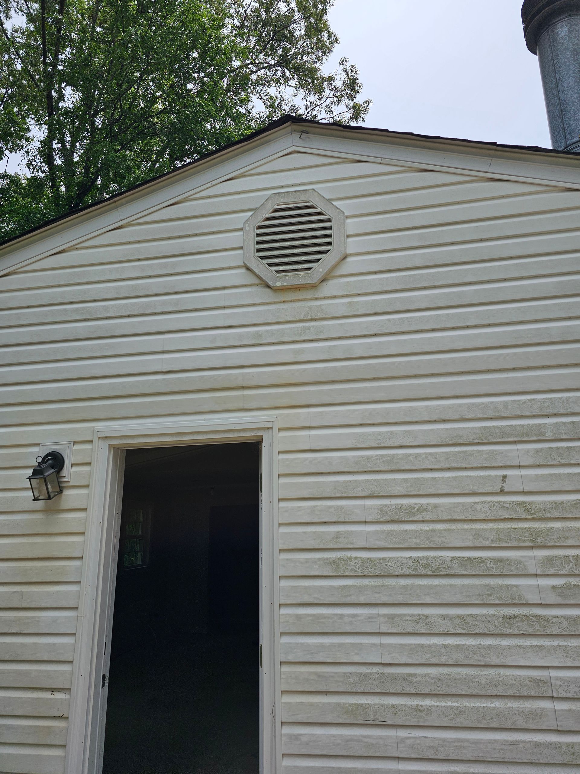 White-sided building with an open door and octagonal vent. Dark stains visible on the siding.