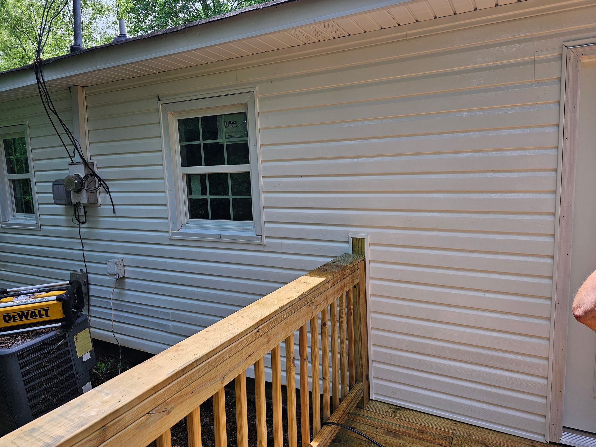 White vinyl-sided house with wooden deck and windows. An electrical box is on the left side.