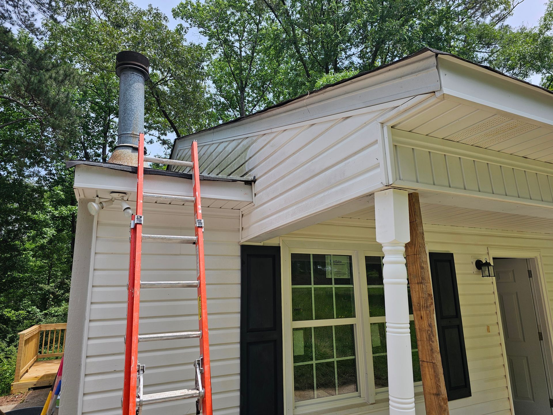 Red ladder leaning against white house roof; chimney and green trees in the background.