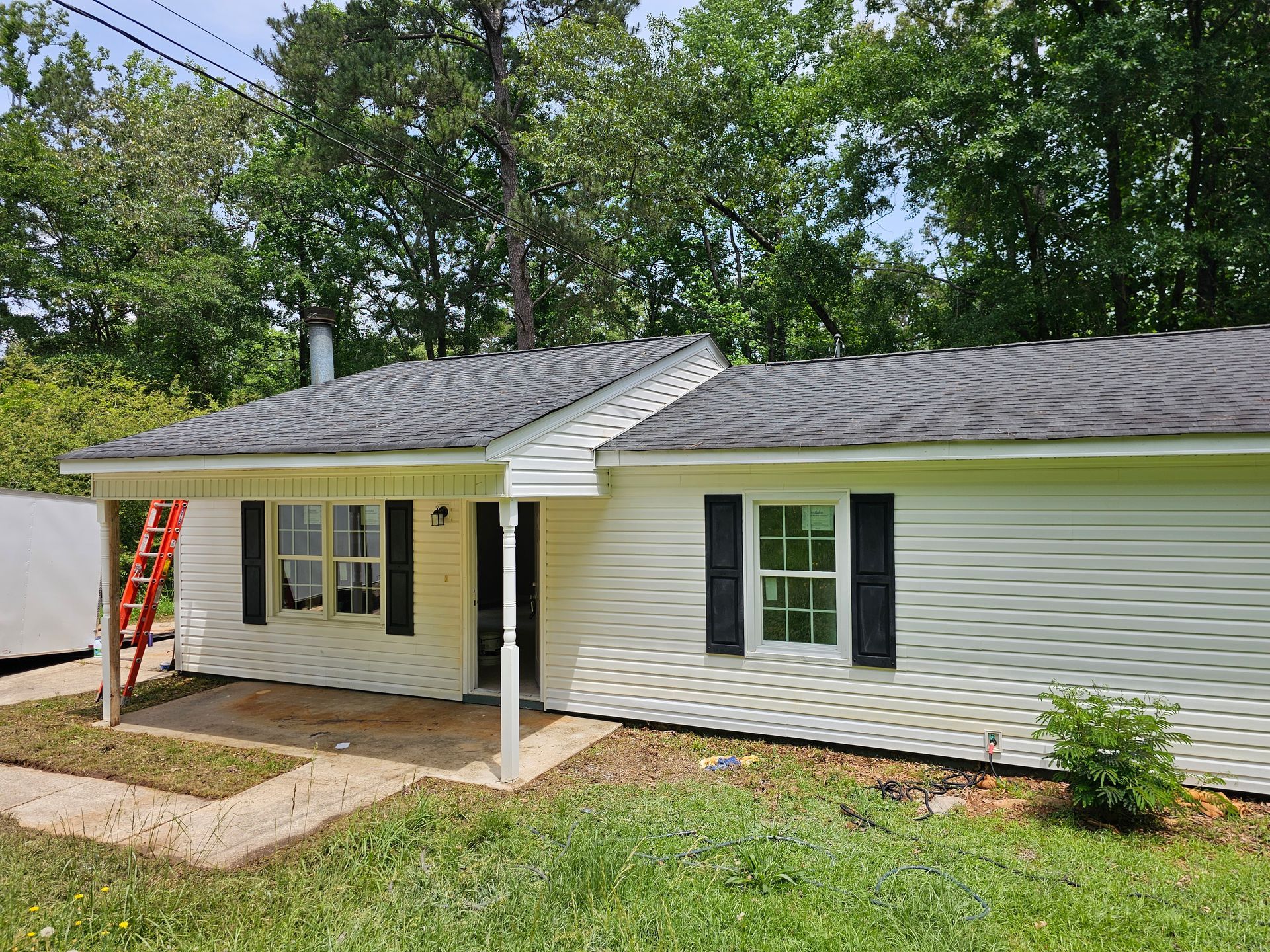 White house with black shutters, gray roof, and green lawn. Red ladder leans on the side.