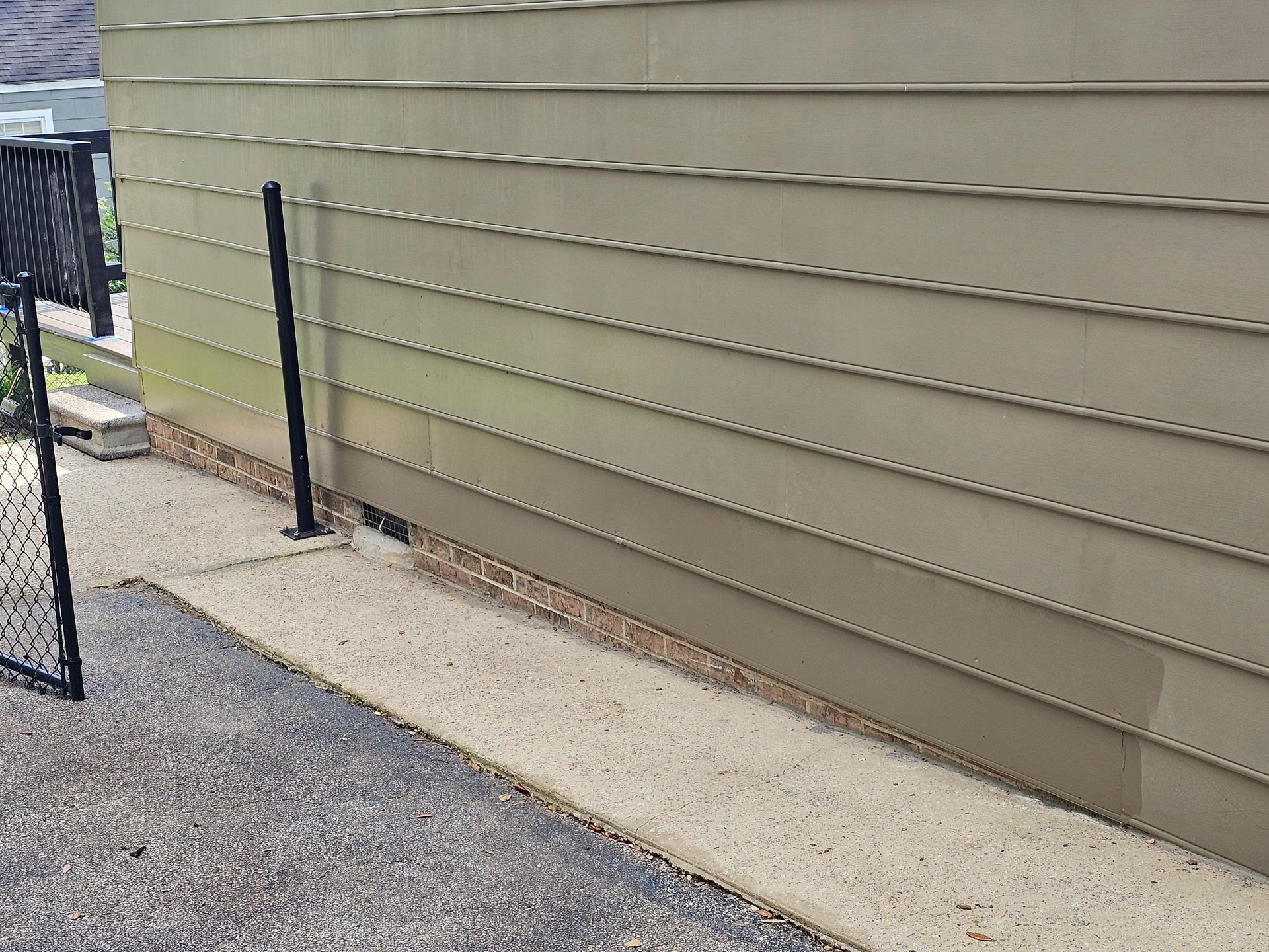 Tan siding on a building with a concrete walkway and a black fence on the left.
